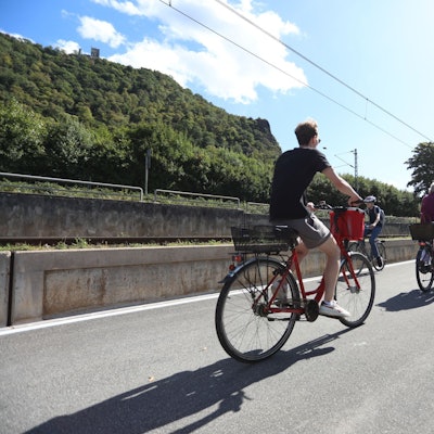 Drei Radfahrer auf einem gut ausgebauten Radweg, im Hintergrund der Drachenfels.