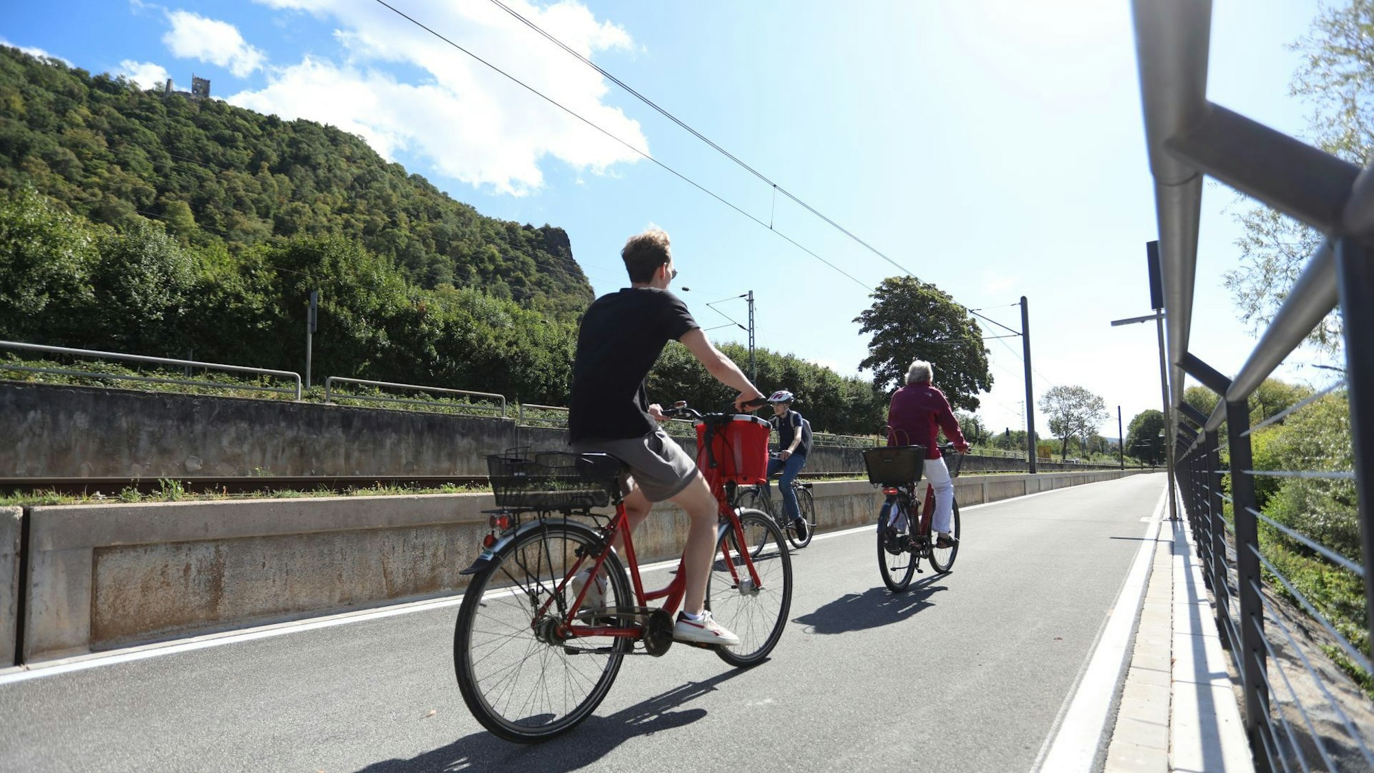 Drei Radfahrer auf einem gut ausgebauten Radweg, im Hintergrund der Drachenfels.