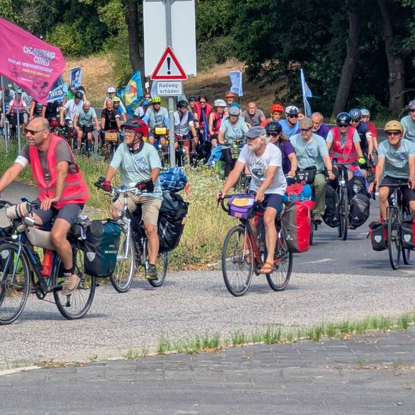 Das Foto zeigt eine große Gruppe auf Fahrrädern, teils mit Flaggen und Bannern.