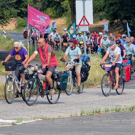 Das Foto zeigt eine große Gruppe auf Fahrrädern, teils mit Flaggen und Bannern.