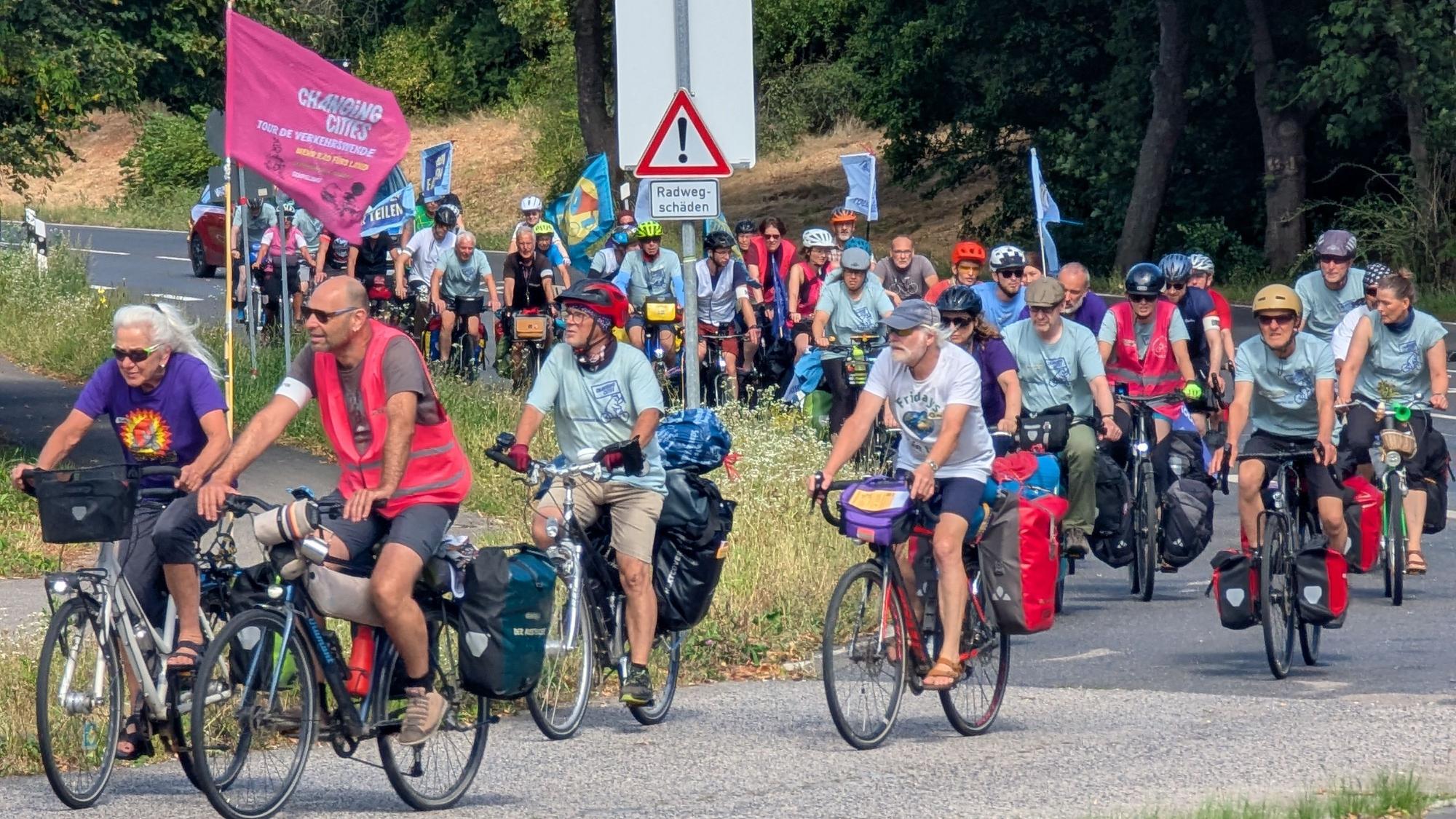 Das Foto zeigt eine große Gruppe auf Fahrrädern, teils mit Flaggen und Bannern.