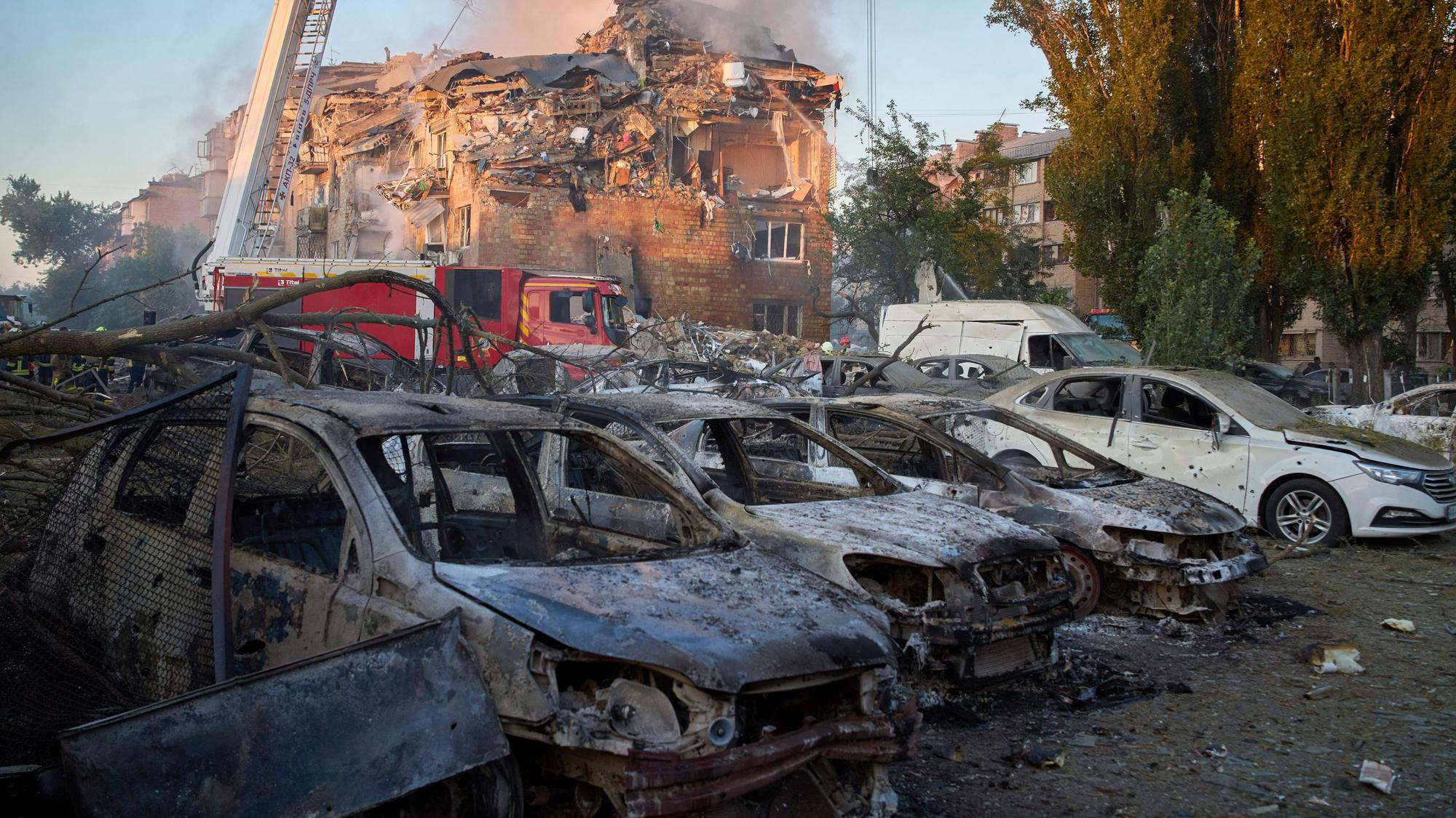 Vor einem zerstörten Wohnhaus in Kyjiw stehen nach dem russischen Großangriff am Donnerstag (27. August) zerstörte Autos.