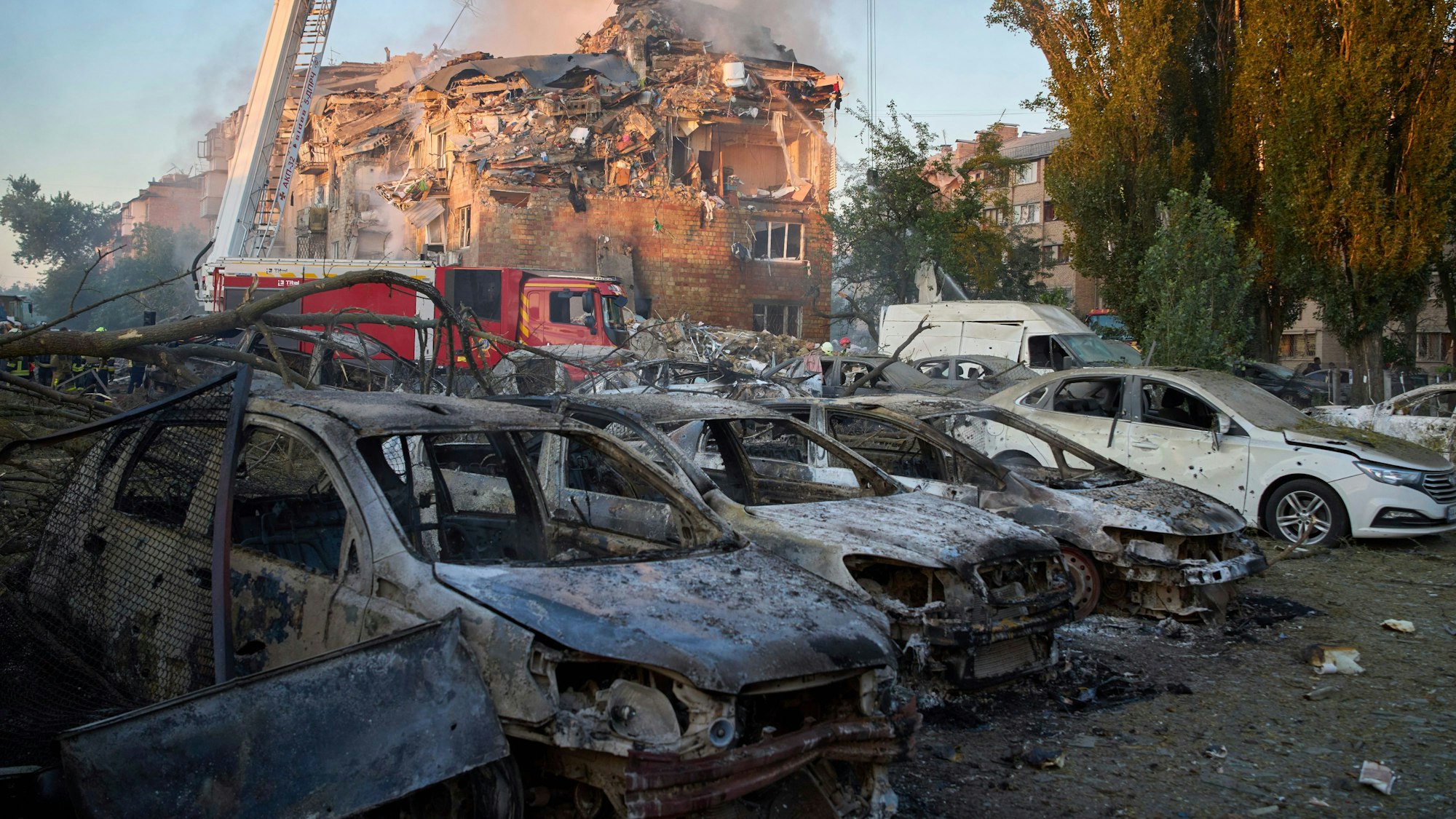 Vor einem zerstörten Wohnhaus in Kyjiw stehen nach dem russischen Großangriff am Donnerstag (27. August) zerstörte Autos.
