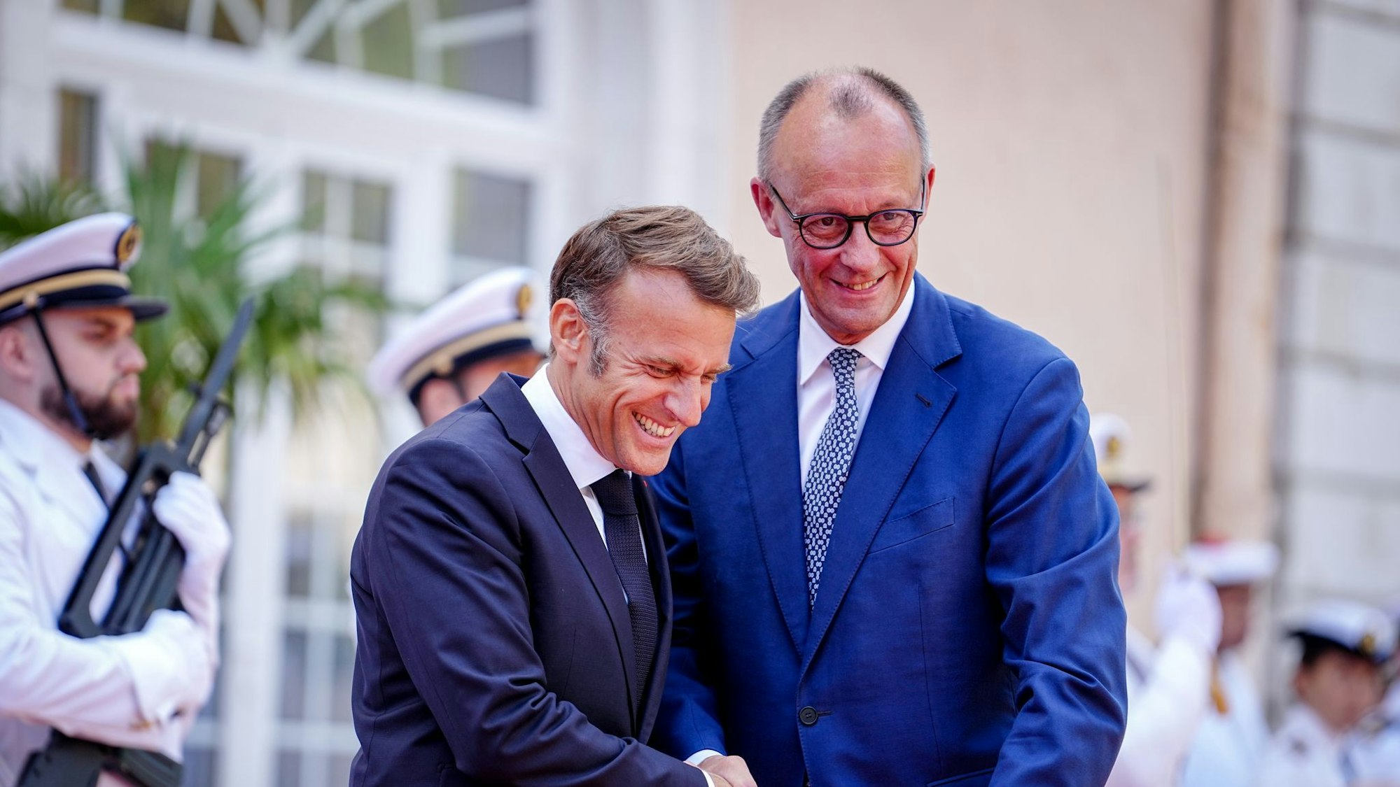 Wie zwei alte Freunde begrüßen sich Macron und Merz vor dem Fort du Cap Brun über der Cote d'Azur.