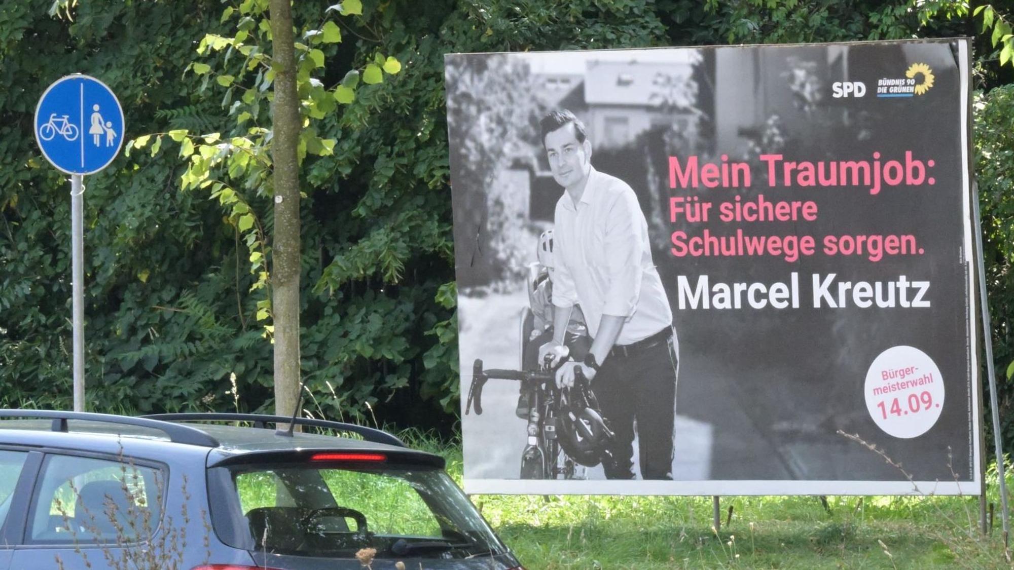 Die Wahlplakate des SPD-Bürgermeisterkandidaten Marcel Kreutz stehen direkt am Radweg. Darauf steht: „Mein Traumjob: Für sichere Schulwege sorgen.“