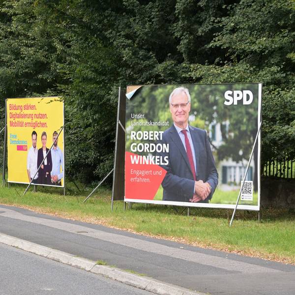 Plakate der CDU, Grünen, FDP und SPD stehen nebeneinander auf der Overather Straße.