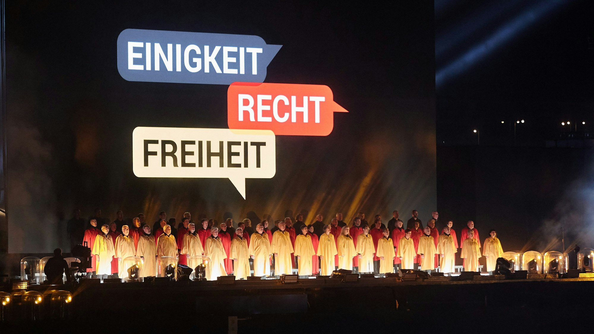 Ein Chor singt während des Abschlusses der Zentralen Feier zum Tag der Deutschen Einheit die Nationalhymne vor den auf den Hintergrund projizierten Worten „Einigkeit“, „Recht“ und „Freiheit“.