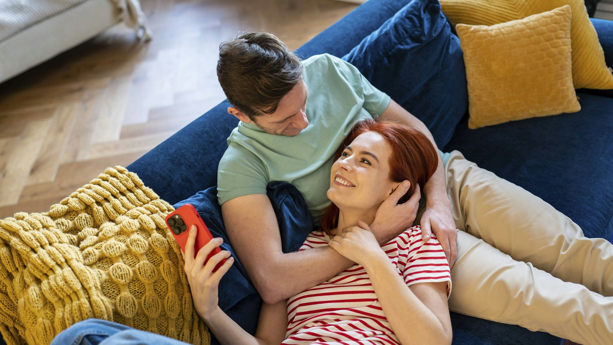 Junges Paar, das auf dem Sofa ruht und von der Zukunft träumt und das Eheleben genießt. Glücklich lächelnd liegt eine Frau auf dem Bauch eines Mannes.