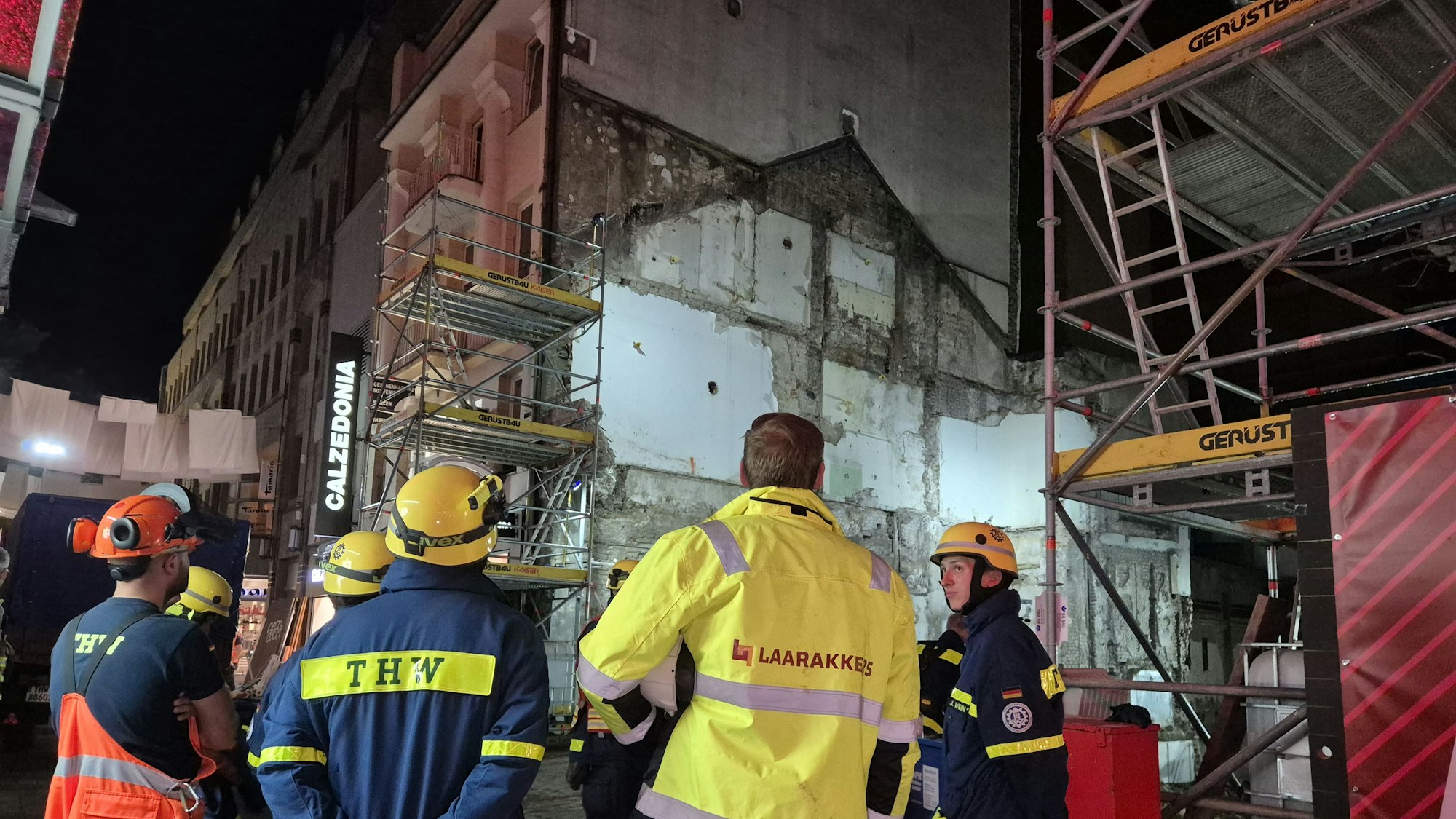 Einsatzkräfte vom Technischen Hilfswerk (THW) und einer Baufirma stehen vor einer Hauswand, die einsturzgefährdet war.