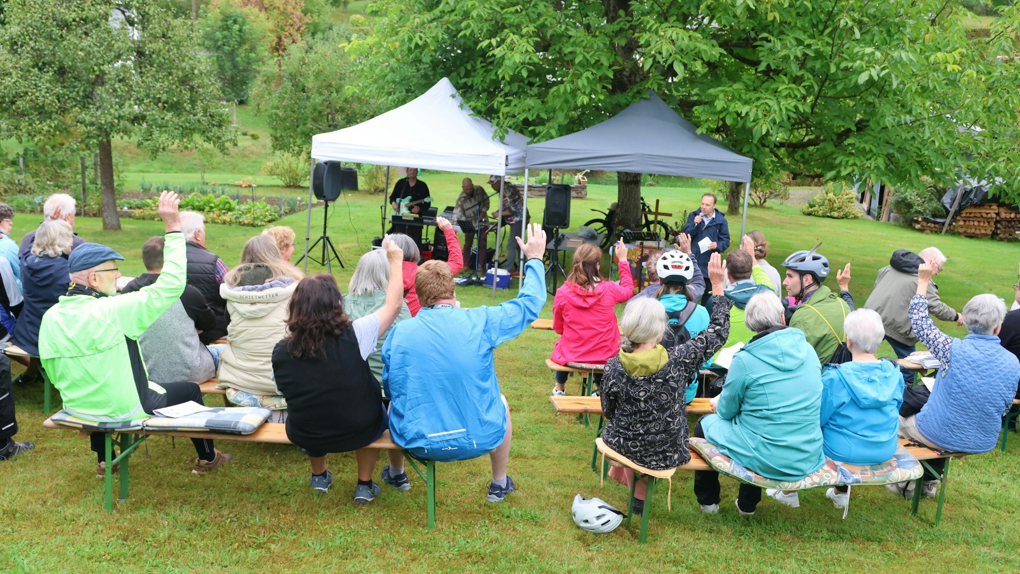 Menschen sitzen auf Bierbänken vor zwei Pavillons.