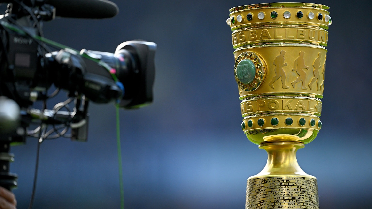 Eine Kamera vor der Siegestrophäe. (zu dpa: «Bayern im Pokal nach Köln - Top-Duell Frankfurt gegen BVB») Foto: Tom Weller/dpa +++ dpa-Bildfunk +++