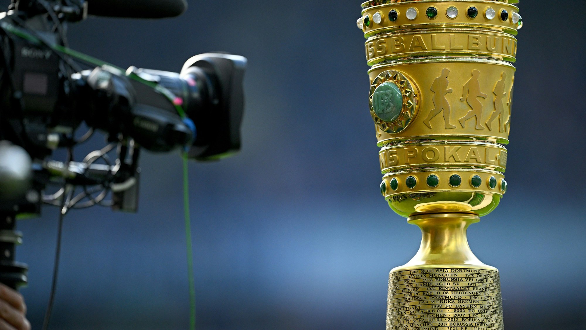 Eine Kamera vor der Siegestrophäe. (zu dpa: «Bayern im Pokal nach Köln - Top-Duell Frankfurt gegen BVB») Foto: Tom Weller/dpa +++ dpa-Bildfunk +++