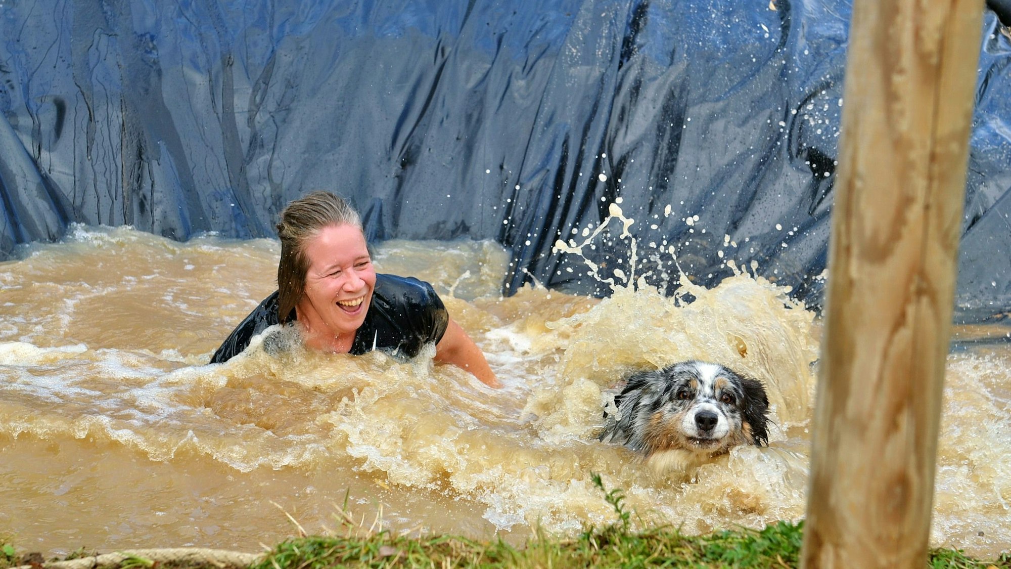 Eine Frau im Wasser schaut lachend auf einen Hund.