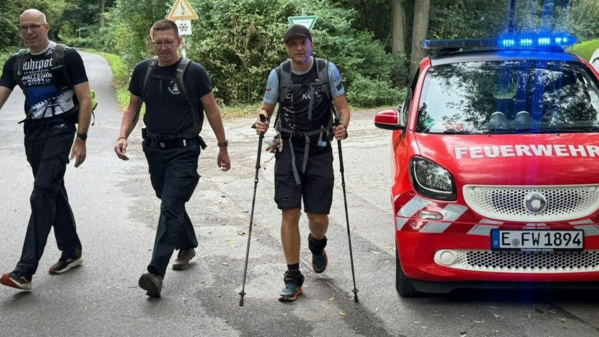 Das Bild zeigt Matthias Stupp mit zwei Männern, die neben ihm wandern. Auch ein Feuerwehrfahrzeug ist zu sehen.