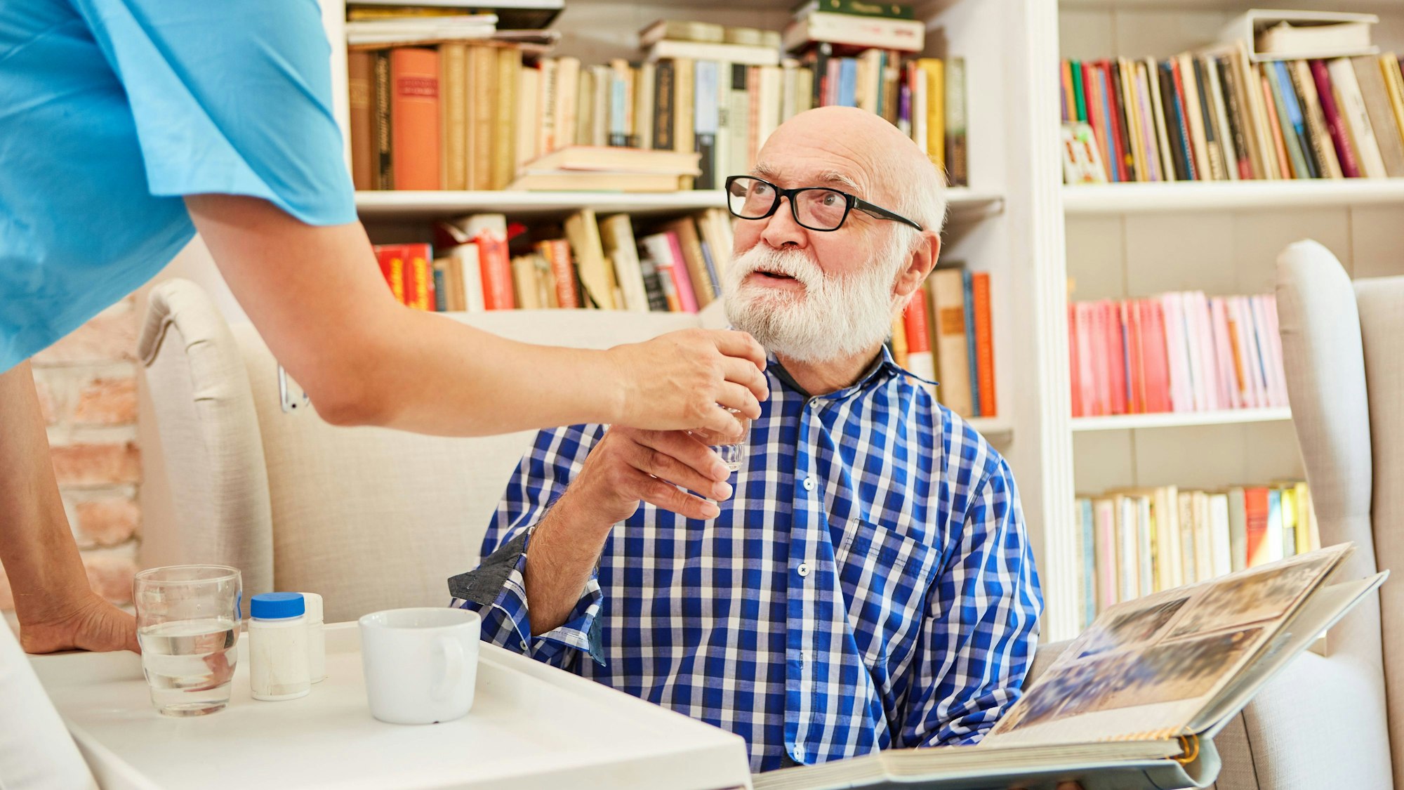 Senior mit Demenz sitzt mit seinem Fotoalbum und bekommt Medikamente.