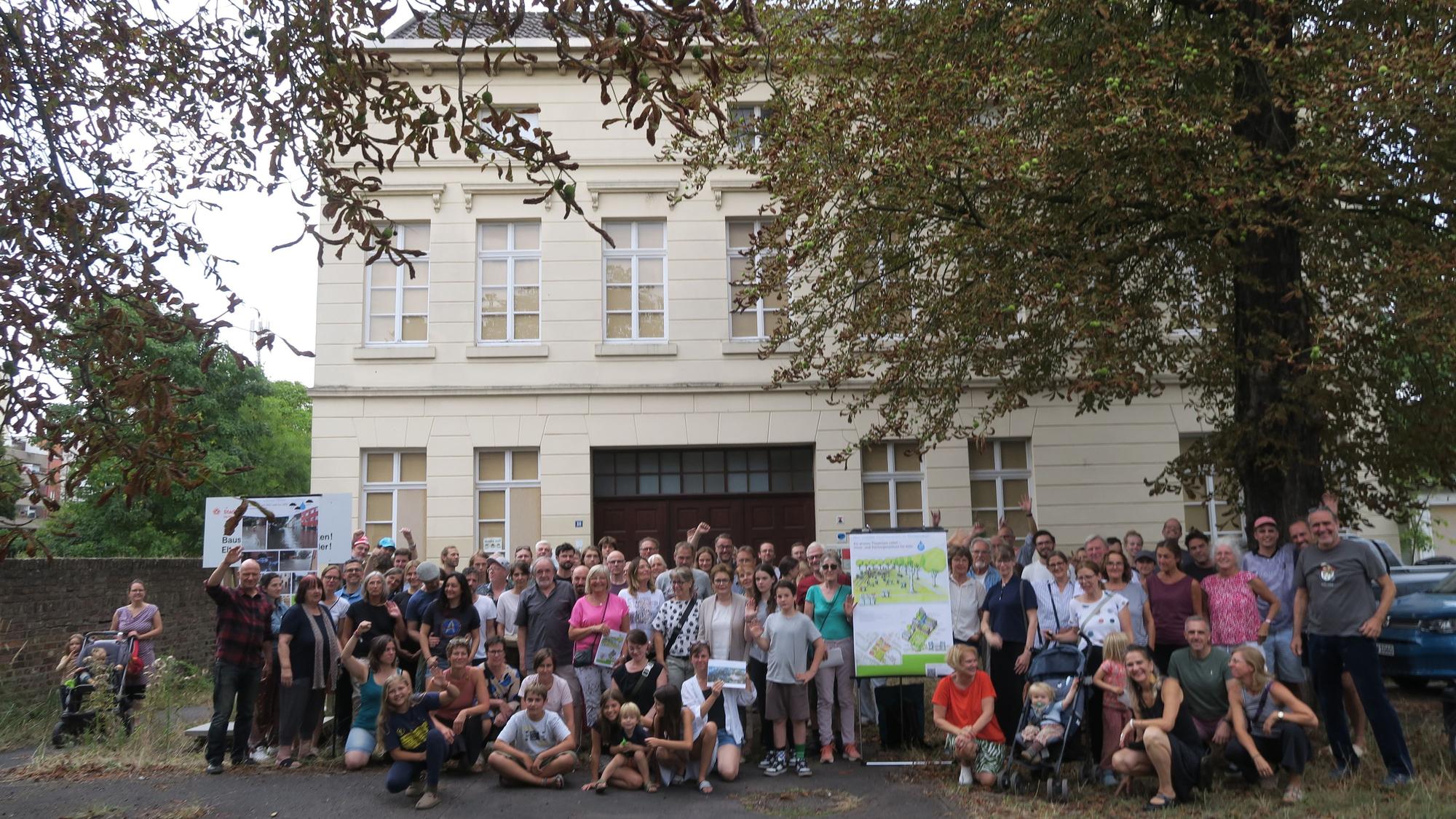 Etwa 100 Leute stehen und hocken vor einem denkmalgeschützten Gebäude.