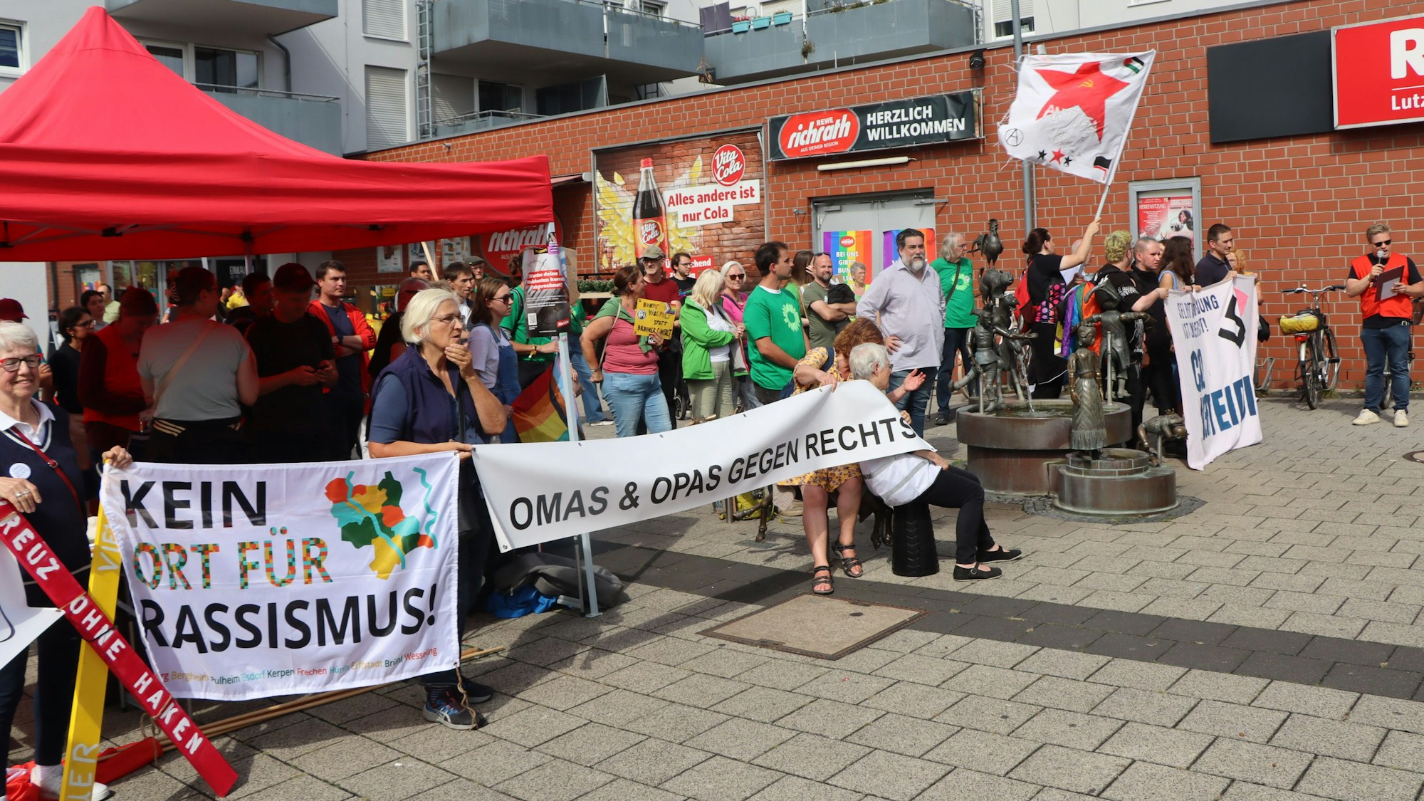 Das Foto zeigt Demonstrierende mit Transparenten vor einem roten Pavillon auf dem Jakob-Eßer-Platz.