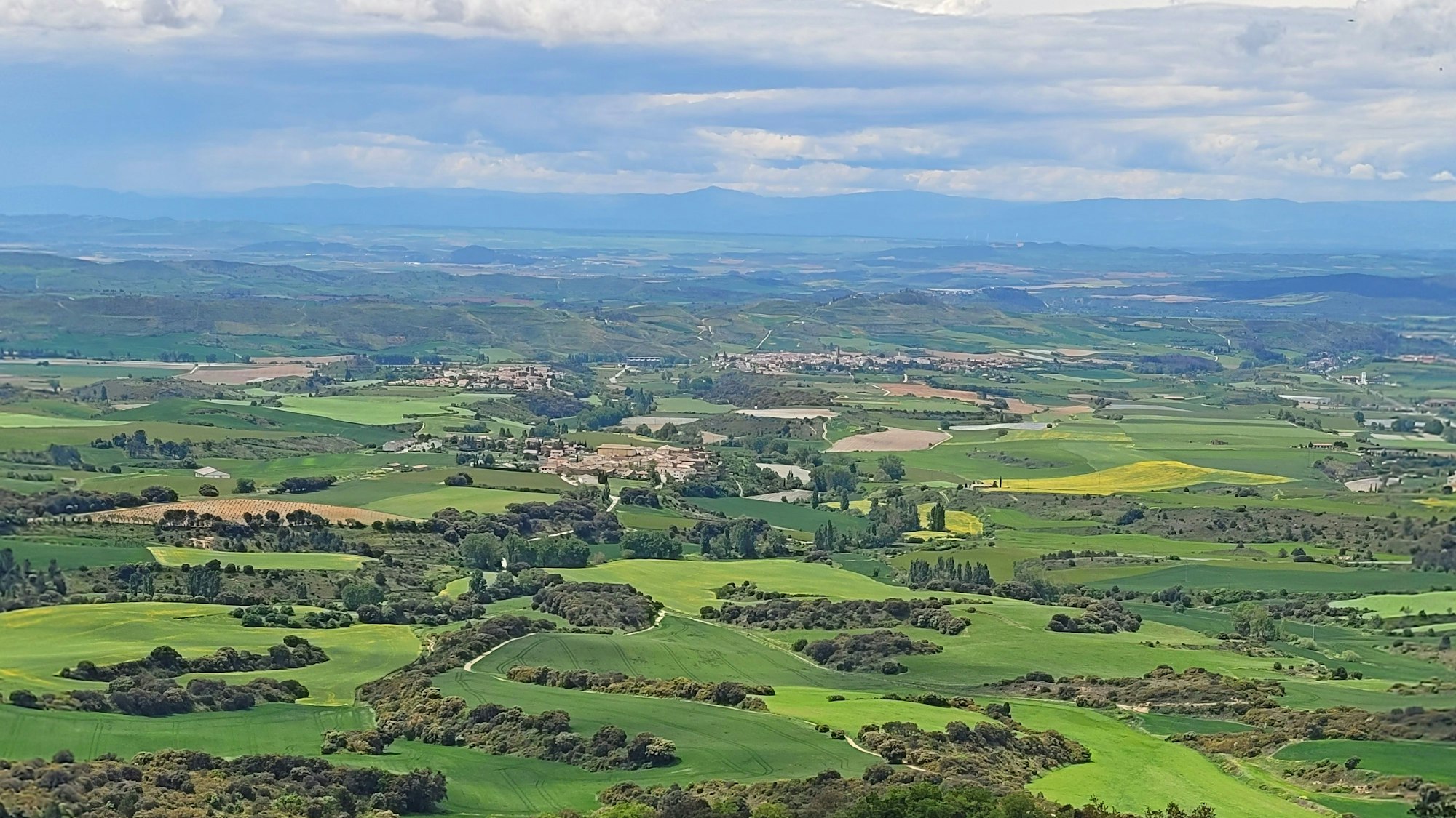 Das Bild zeigt eine Landschaft mit Wäldern und Wiesen, im Hintergrund Ortschaften und eine Bergkette.