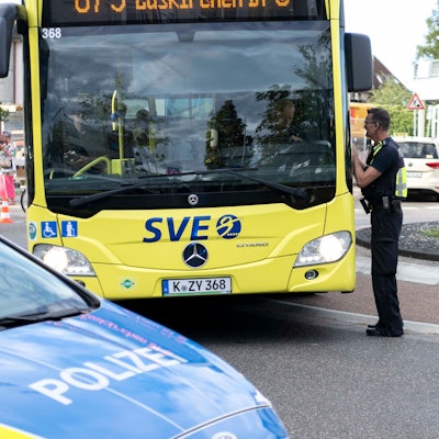 Das Bild zeigt einen Polizisten, der einem Busfahrer erklärt, dass die Straße gesperrt ist.