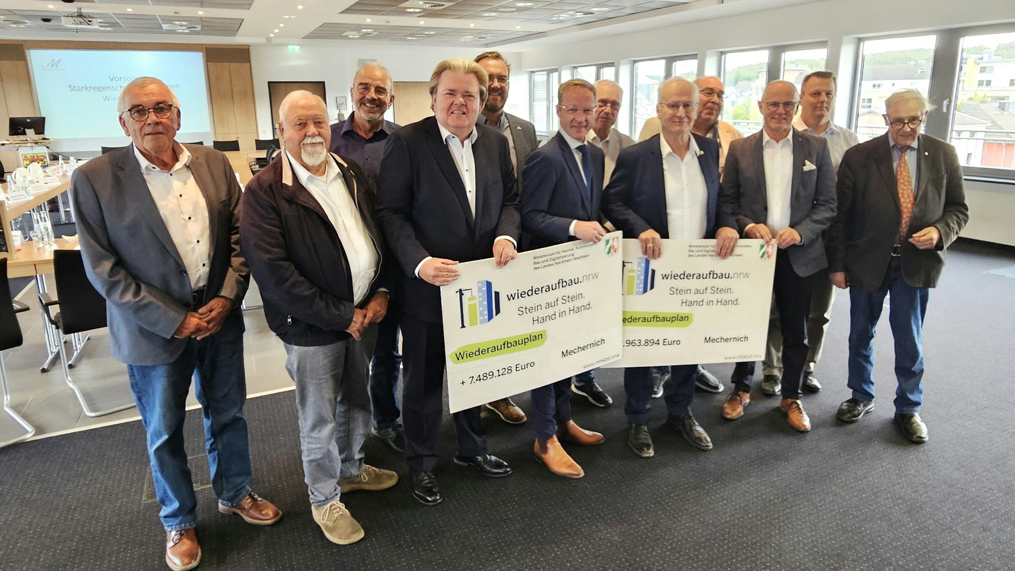 Zwölf Männer stehen nebeneinander und präsentieren zwei symbolische Förderbescheide.