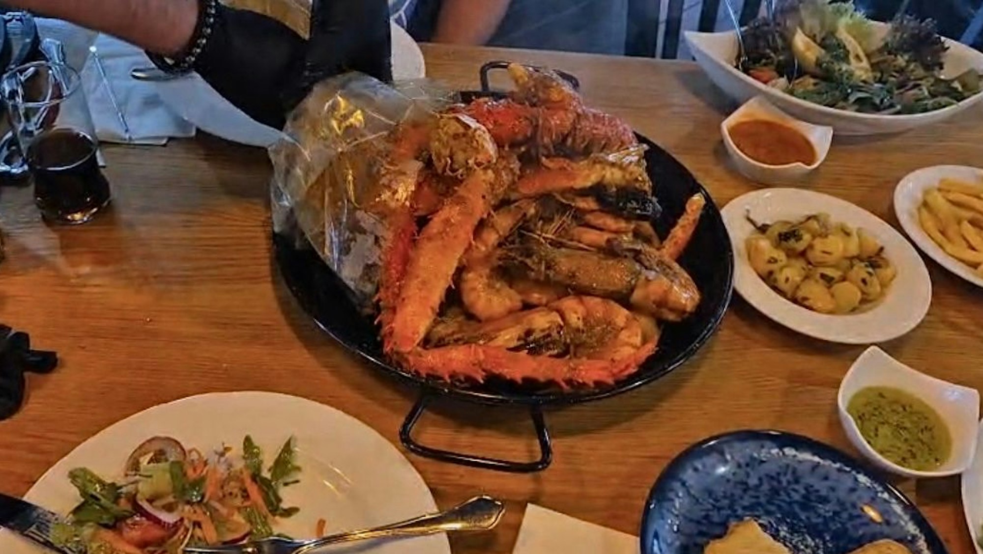 Der Kellner entleert den Beutel nicht auf dem Tisch, sondern in einer großen Paella-Pfanne.