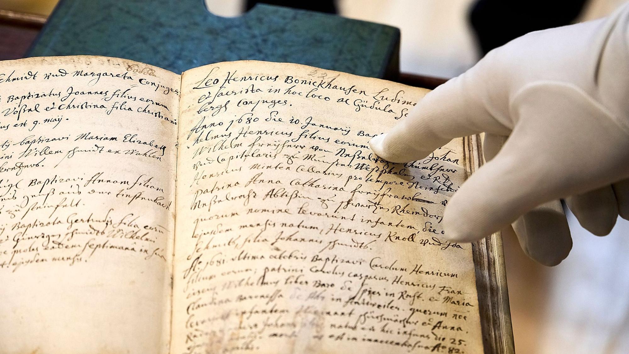 Eine Hand, die in einem weißen Handschuh steckt, zeigt auf einer Stelle in einer alten Schrift, die auf die Vorfahren von Gustave Eiffel verweist.
