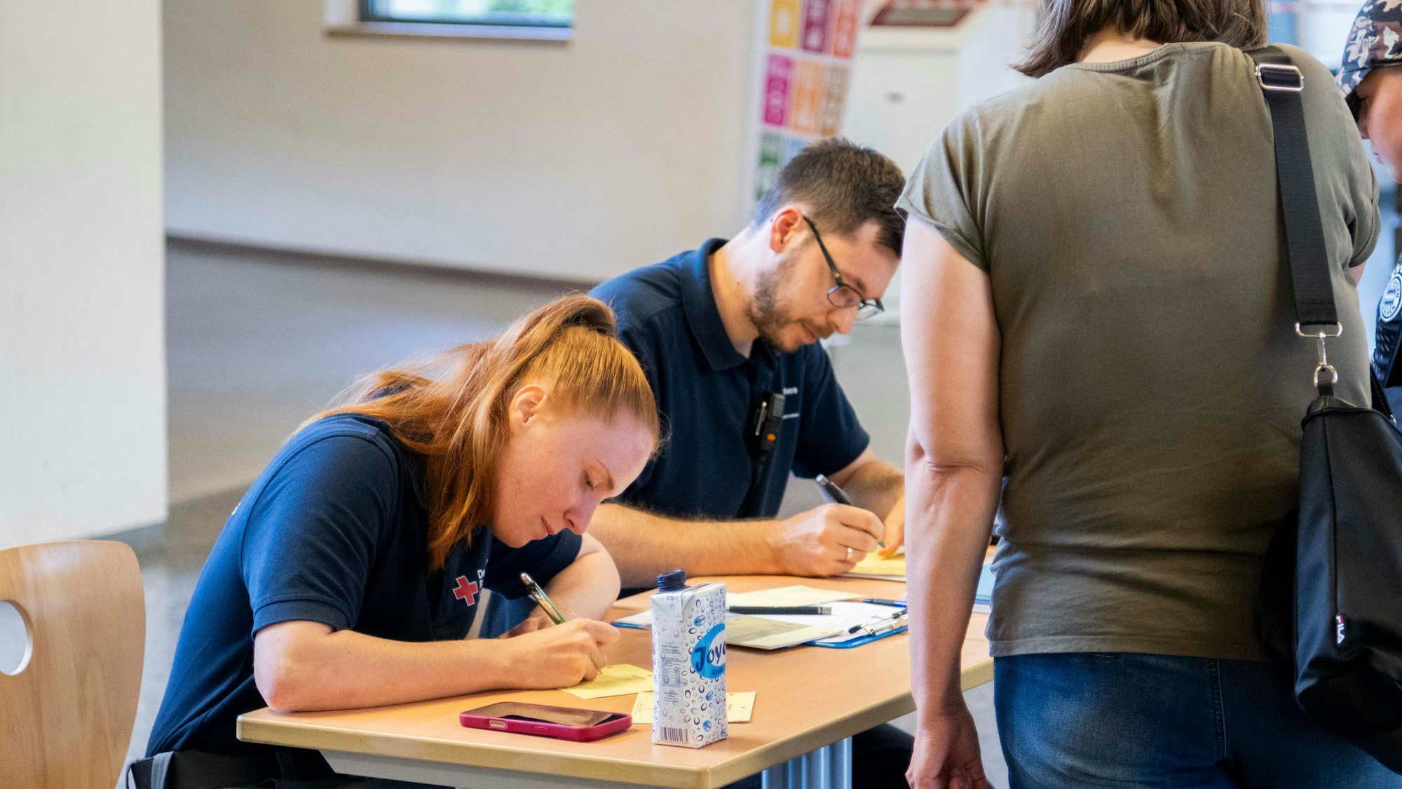 Das Bild zeigt zwei Mitarbeitende des DRK, die die Personalien von einer Mutter und ihrem Sohn erfassen.