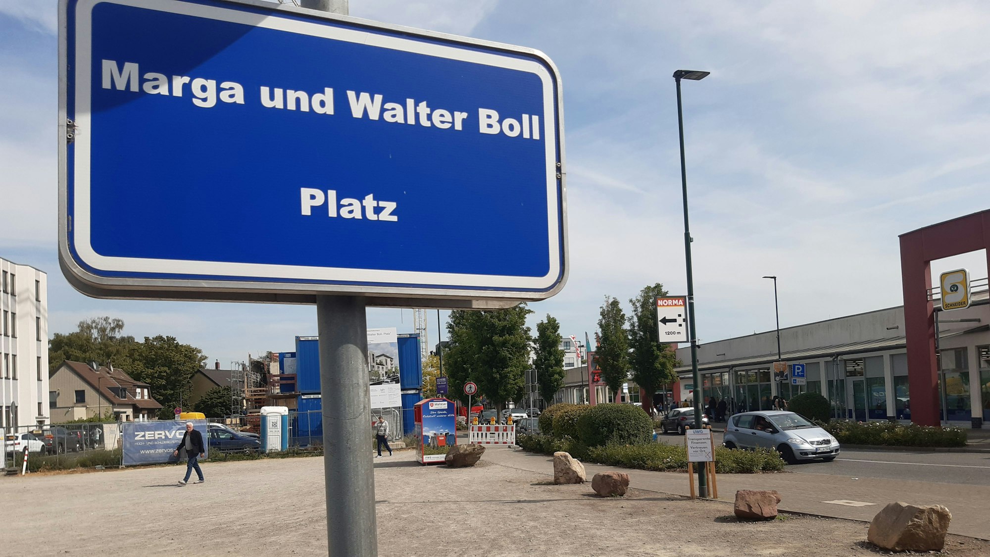 Das Bild zeigt ein Schild mit der Aufschrift „Marga-und-Walter-Boll-Platz“, im Hintergrund der recht kahle Platz.