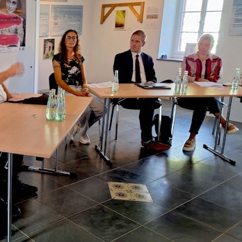 Sechs Menschen sitzen zusammen an einer Tischgruppe und diskutieren.