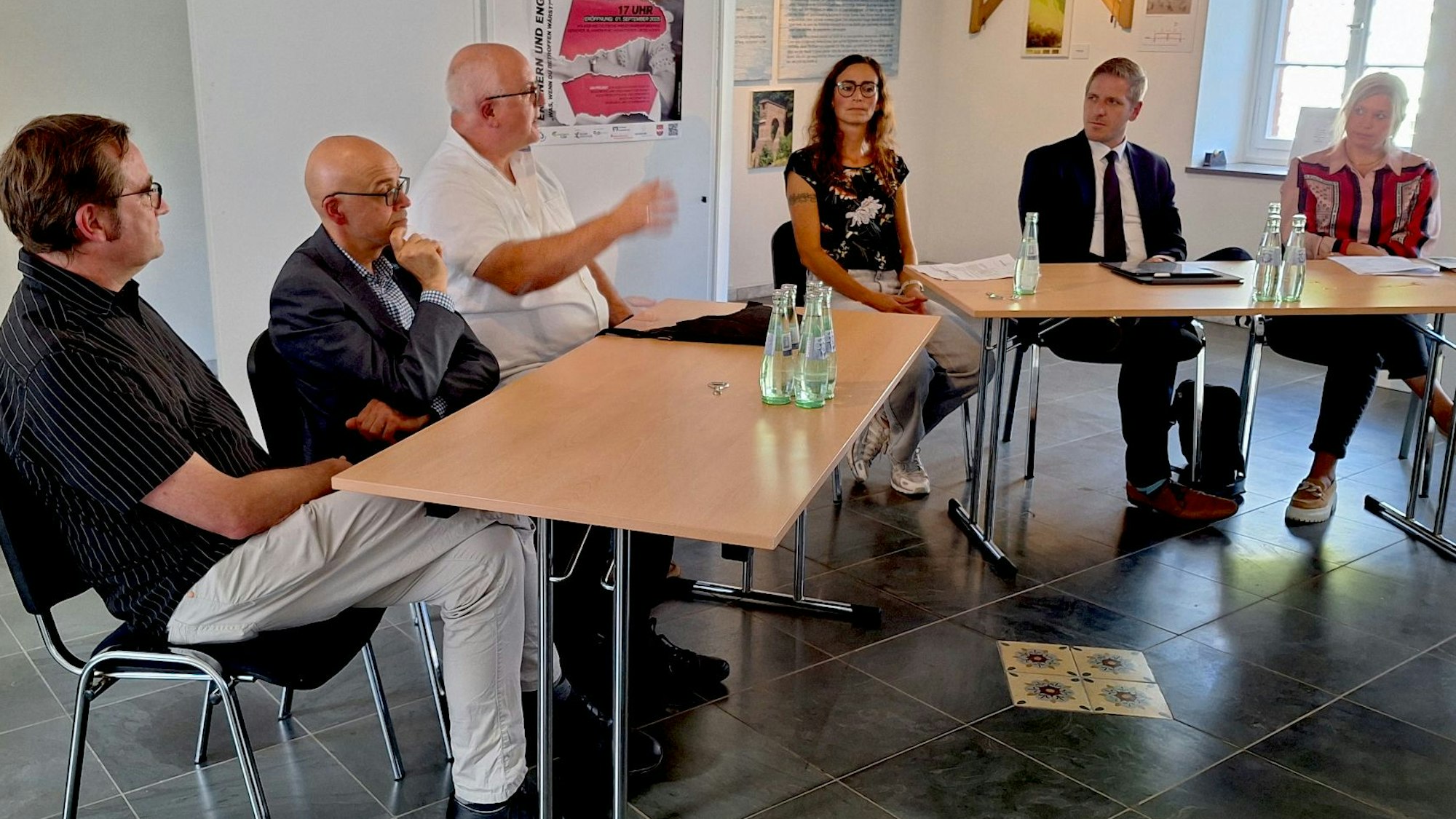 Sechs Menschen sitzen zusammen an einer Tischgruppe und diskutieren.