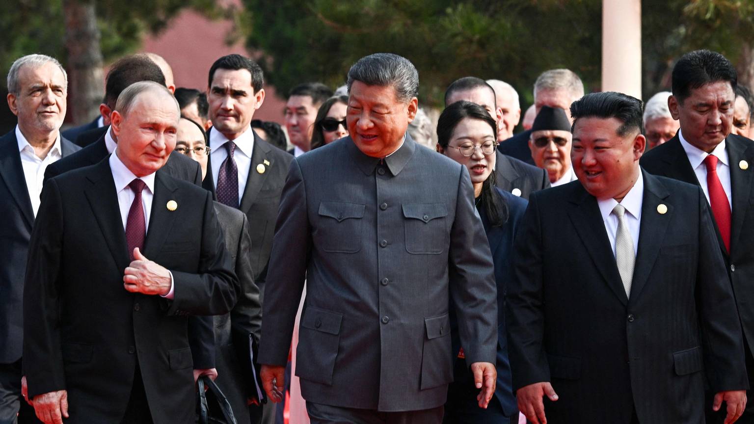 Putin, Xi und Kim gehen lächelnd nebeneinander her.