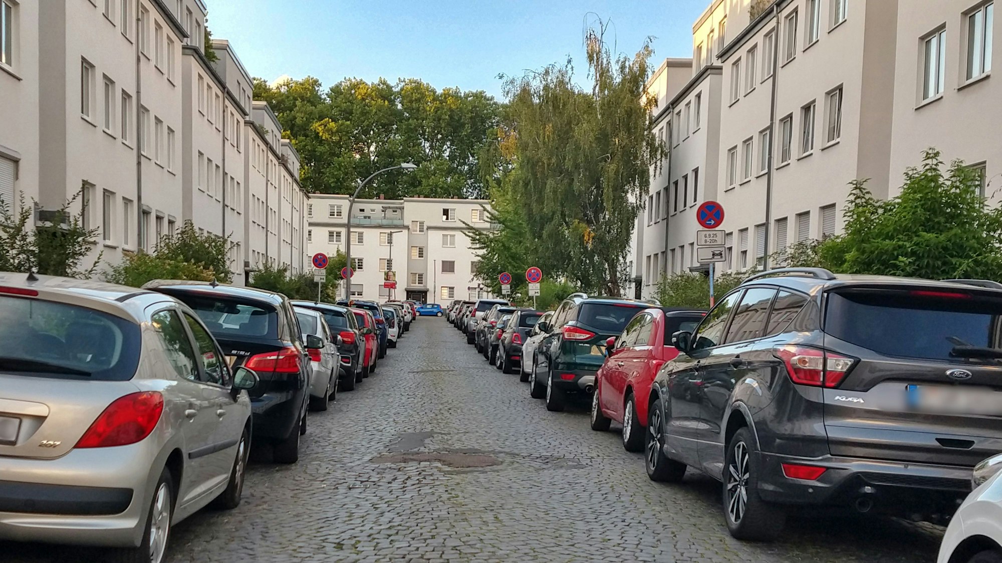 Eine enge, lange Straße, auf der links und rechts viele Autos parken.