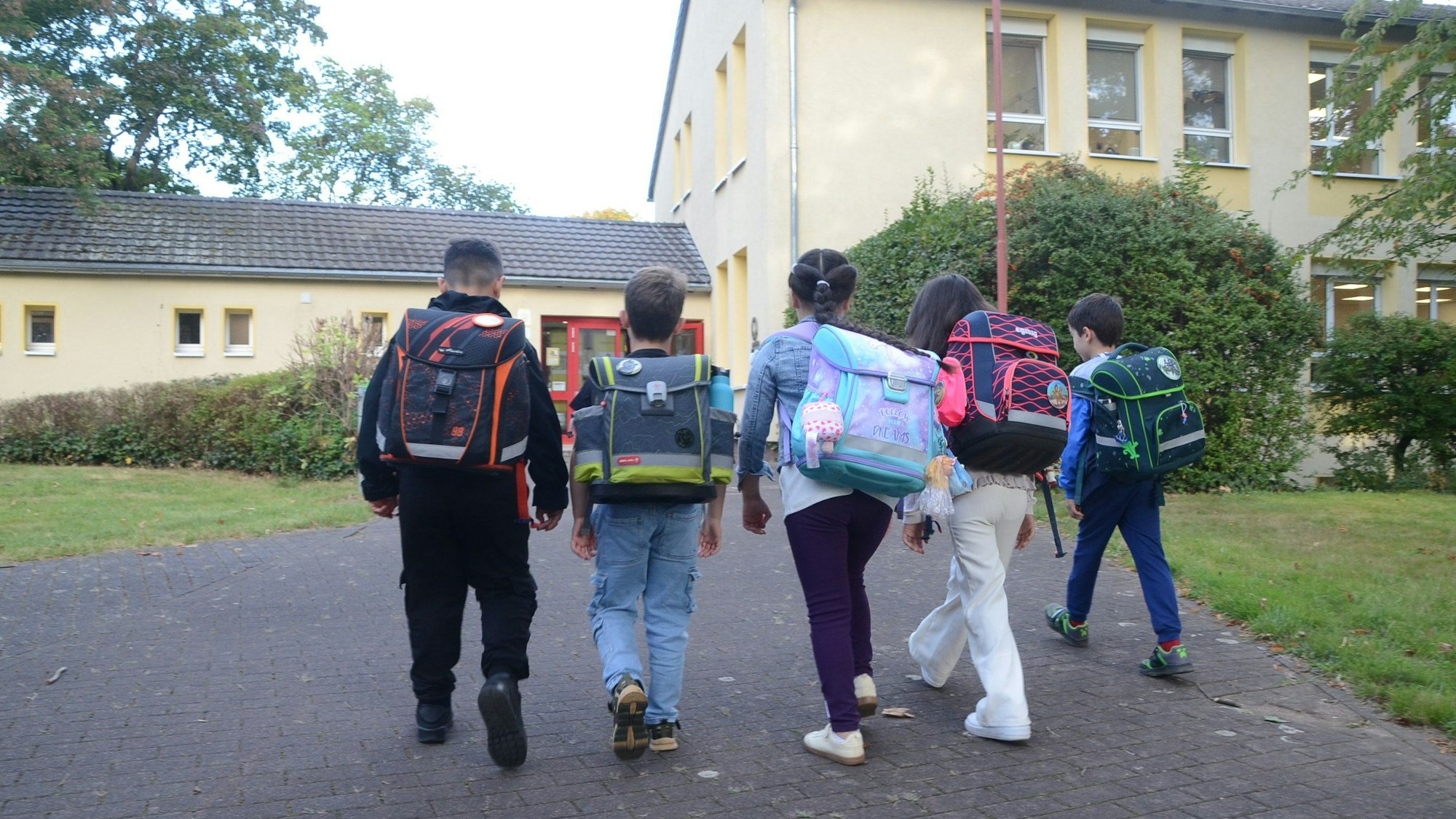 Grundschulkinder laufen auf ein Schulgebäude zu.