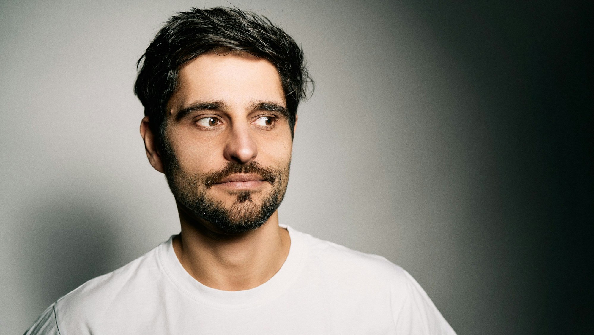 Ein junger Mann mit Bart blickt skeptisch.