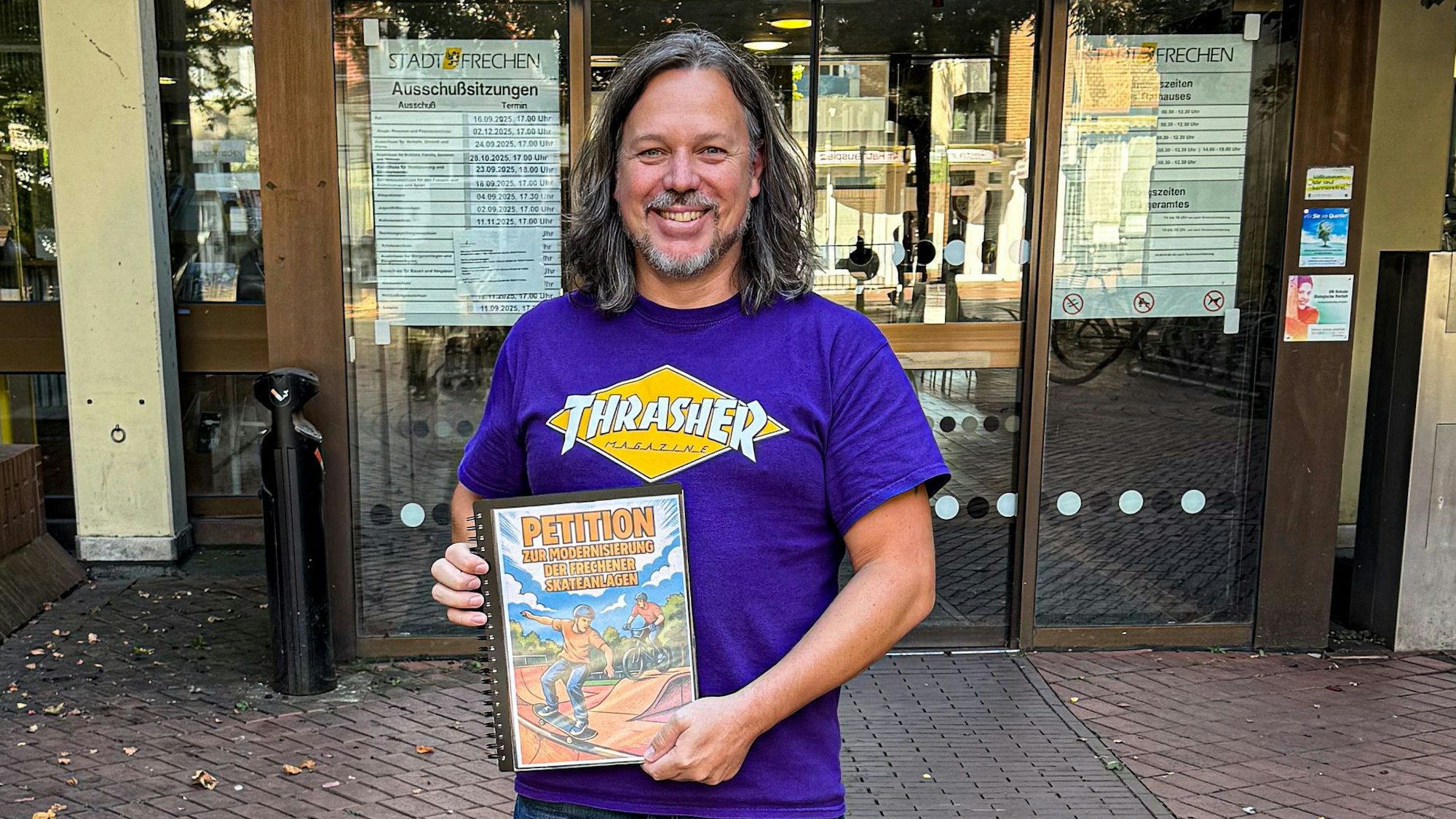 Auf dem Bild ist ein Mann mit einer Unterschriftenmappe vor dem Rathaus zu sehen.