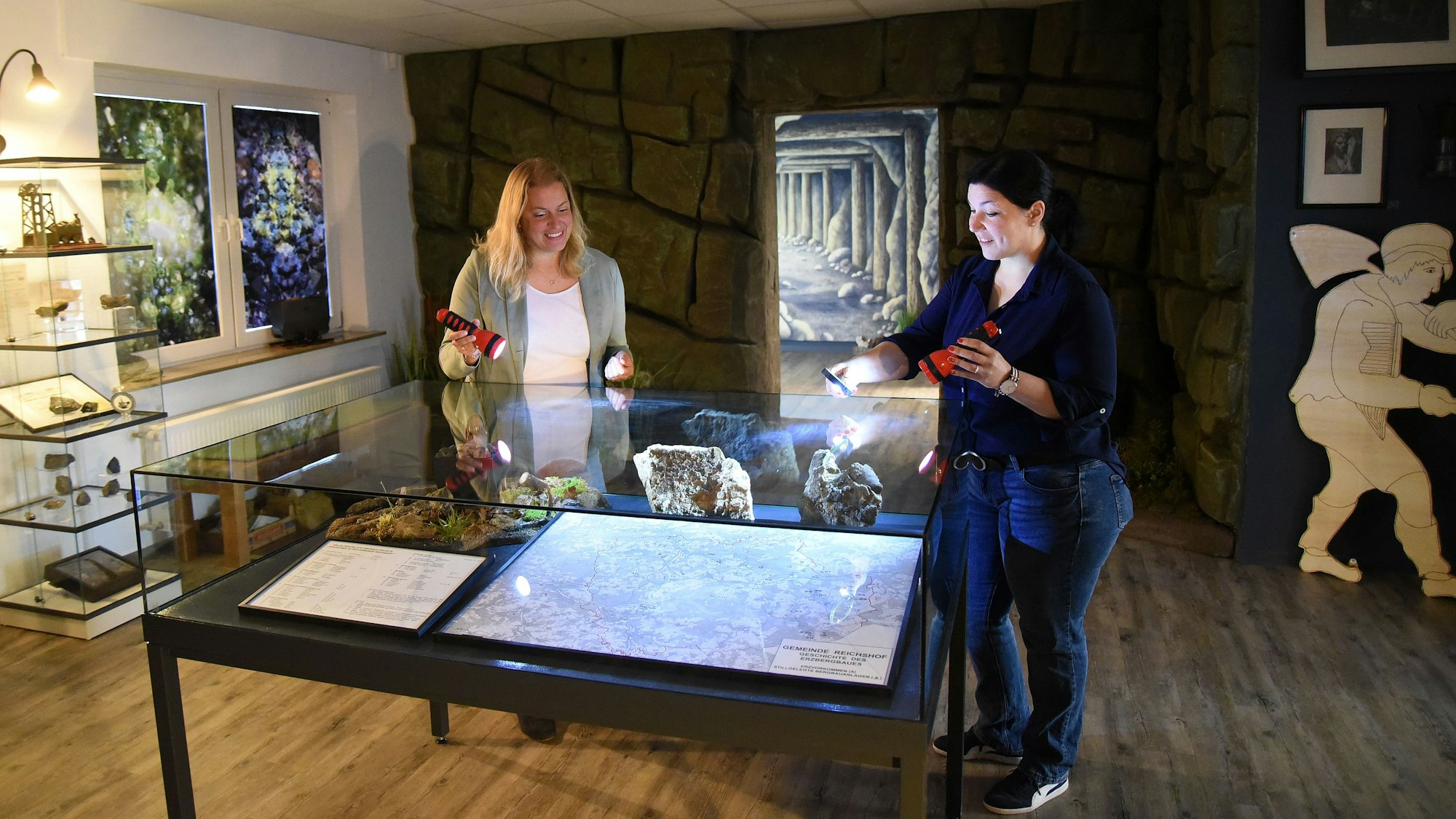 Katja Wonneberger-Kühr (links) und Sarah-Sophie Riedel beleuchten mit Taschenlampen die Übersichtskarte im ersten der beiden Ausstellungsräume. Im weiteren Verlauf warten Grubenwerkzeuge, Erinnerungsstücke und auch Münzen aus Wildberger Silber auf die Besucher.