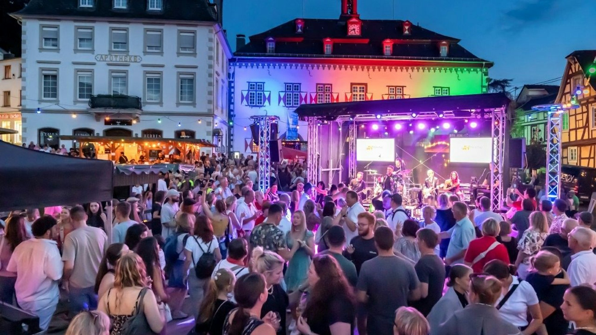 Menschen auf einem Platz, im Hintergrund eine Bühne, auf der eine Band spielt.