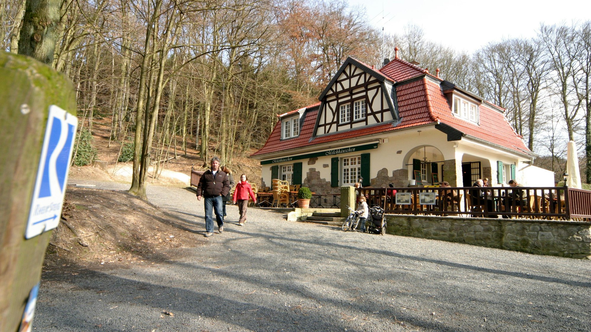 Hinter einer Wegemarkierung des Rheinsteigs ist das Lokal Milchhuschen im Siebengebirge zu sehen.