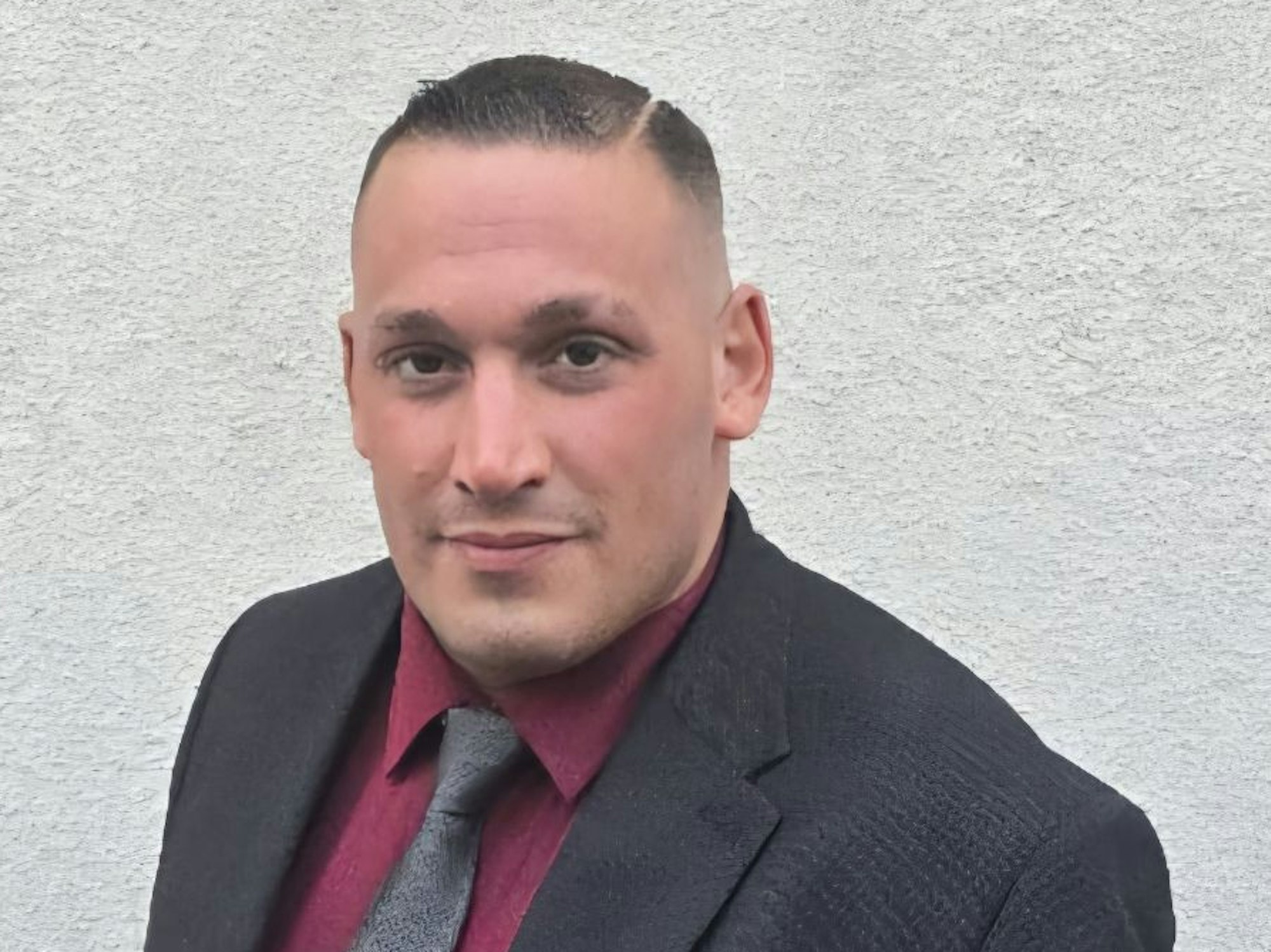 Simon Müller steht im Anzug vor einer Wand.