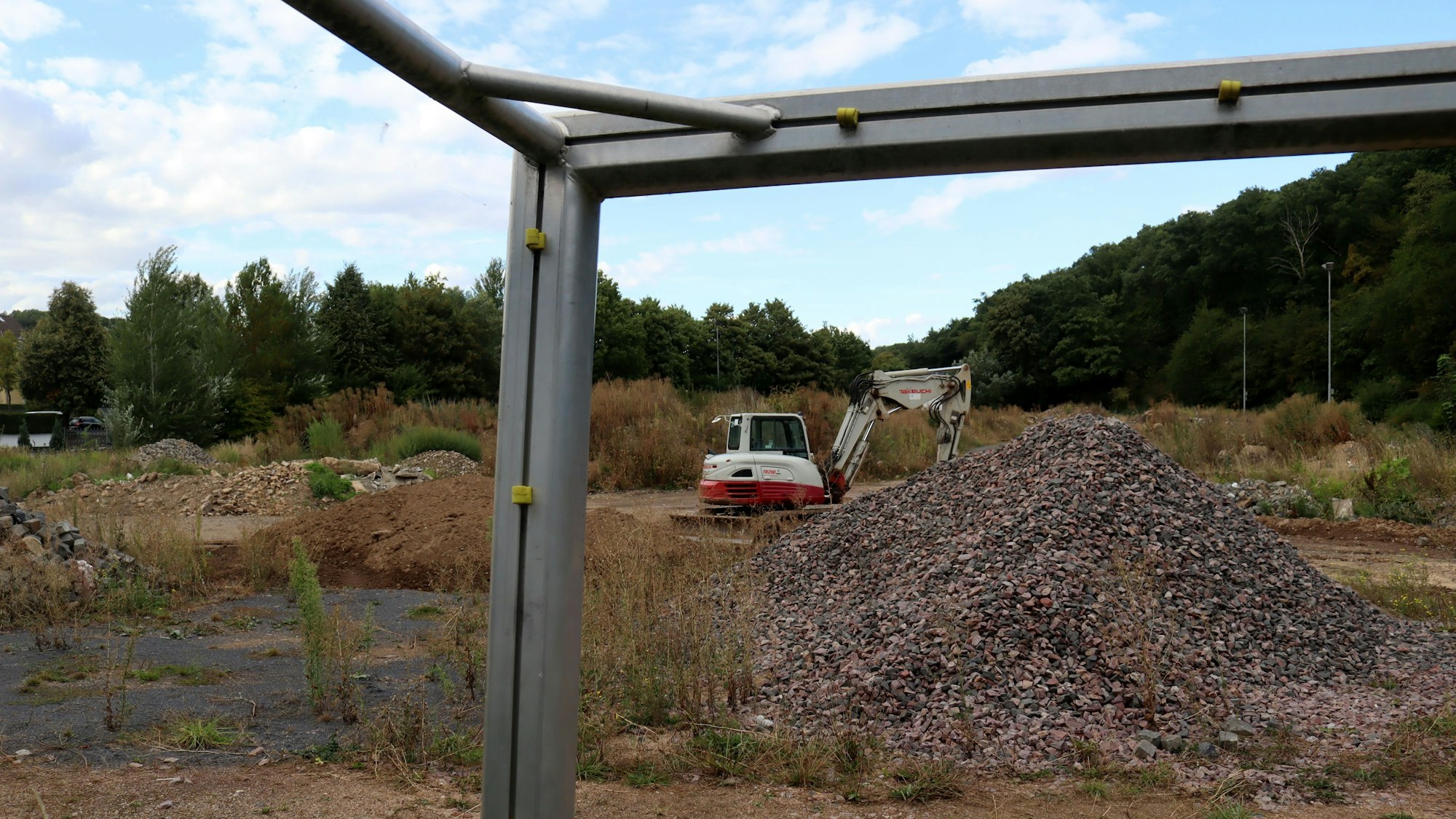 Das Bild zeigt den Sportplatz in Bad Münstereifel, der seit der Flutkatastrophe als Ablagestätte für Schutt genutzt wird. Das Foto wurde durch das Fußballtor hindurch gemacht, im Torwinkel befindet sich ein Bagger.