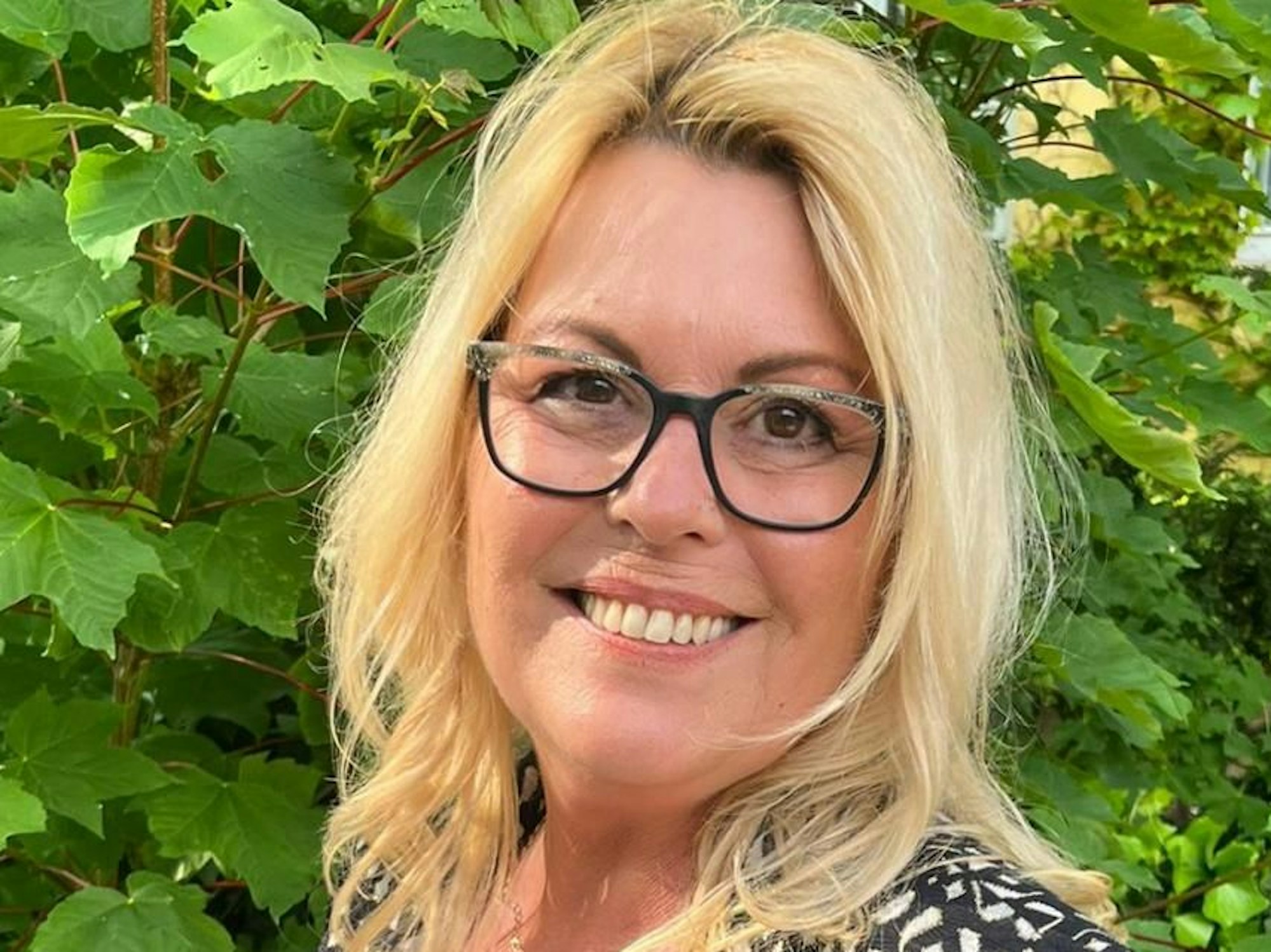 Iris Lafazanis steht im Grünen und lächelt.