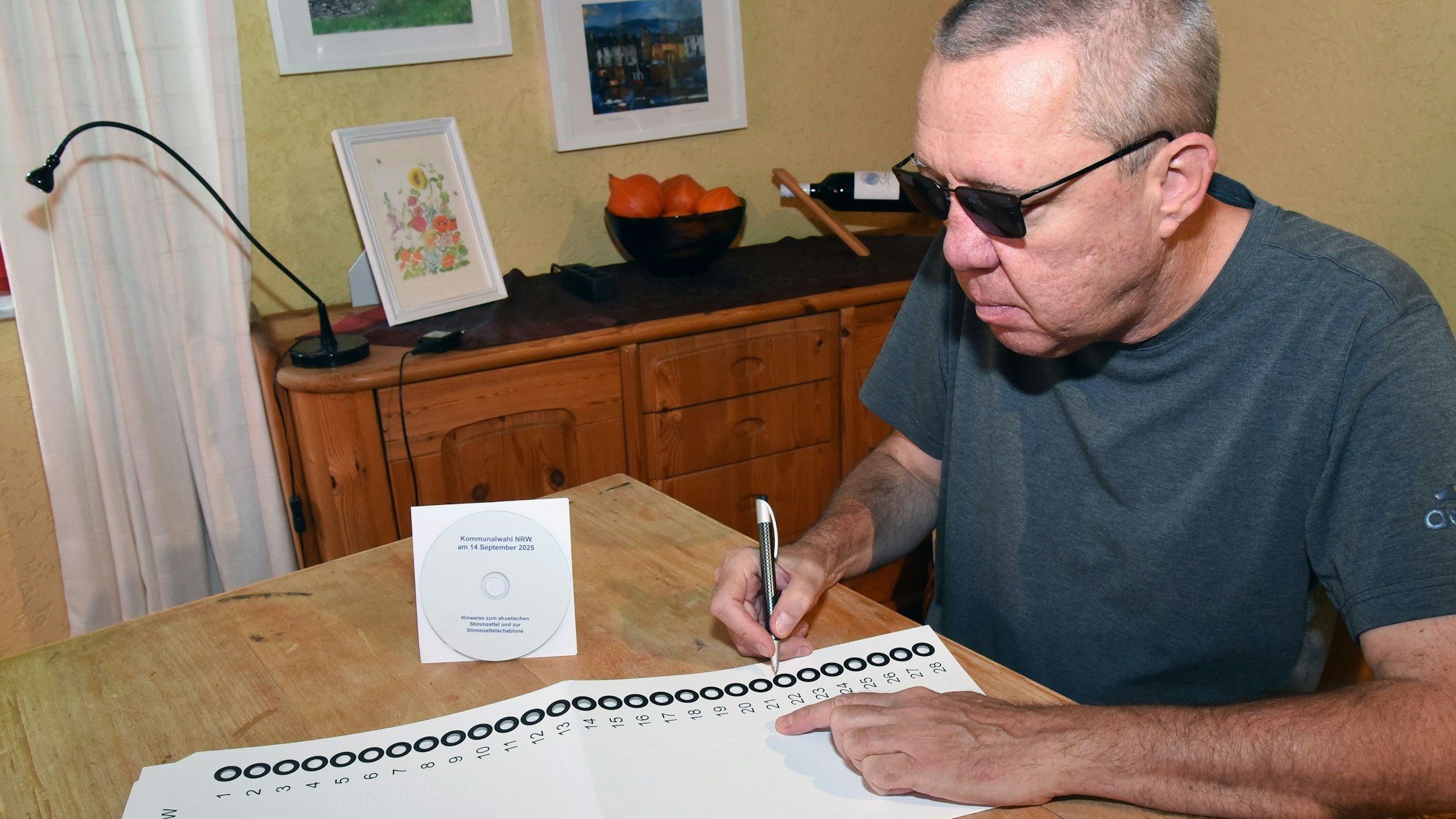 Zu sehen ist ein blinder Mann mit der Wahlschablone NRW und einer CD mit Informationen zur Hotline, die den Stimmzettel vorliest.