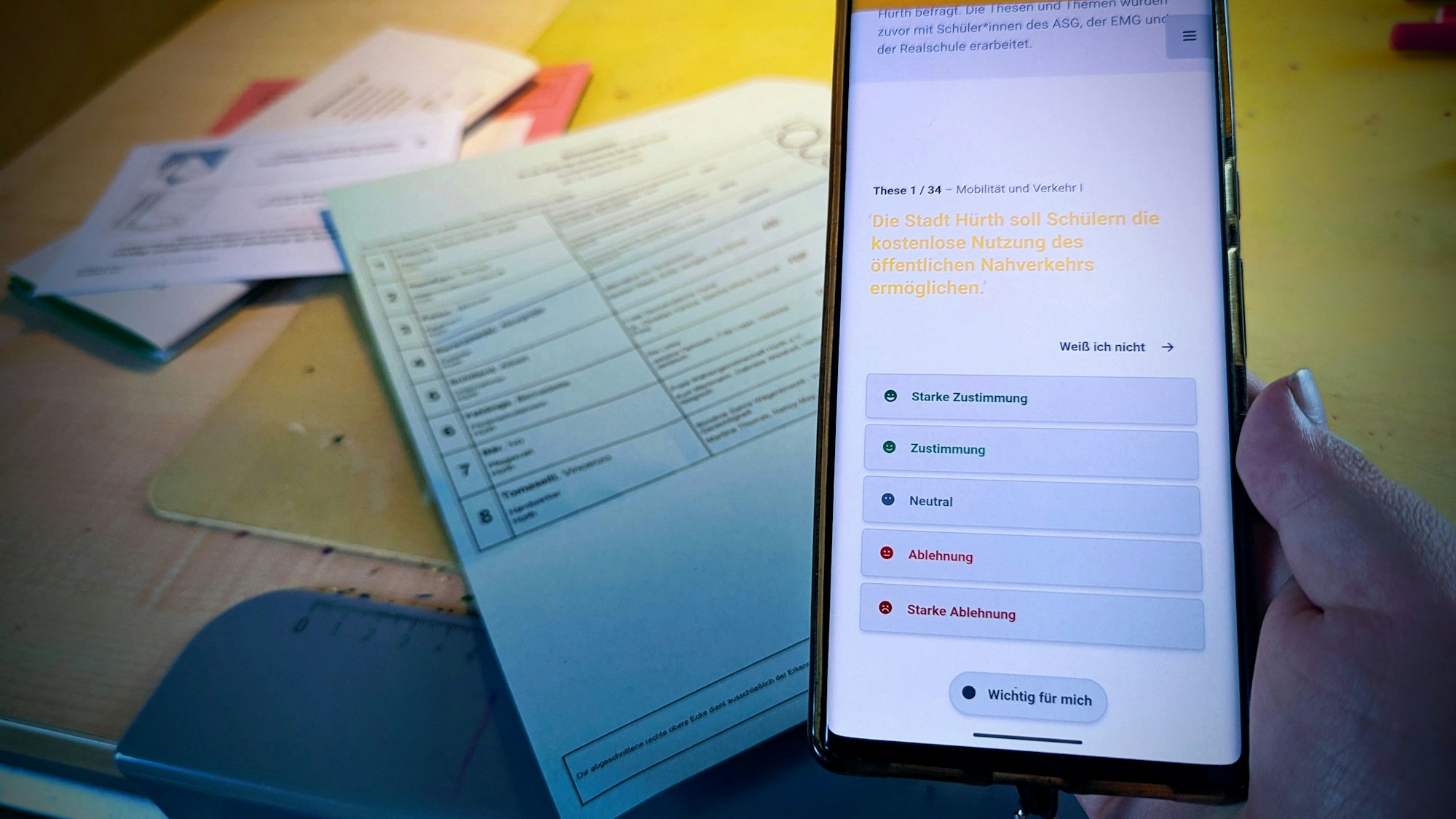 Das Foto zeigt den Wahl-O-Mat auf einem Mobiltelefon, im Hintergrund ein Stimmzettel.