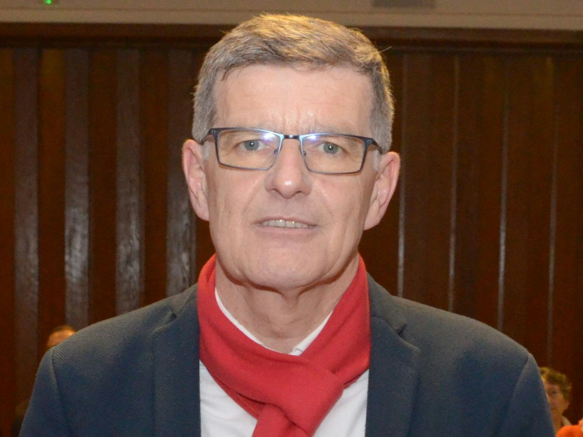 Michael Höllmann trägt einen Anzug und einen roten Schal.