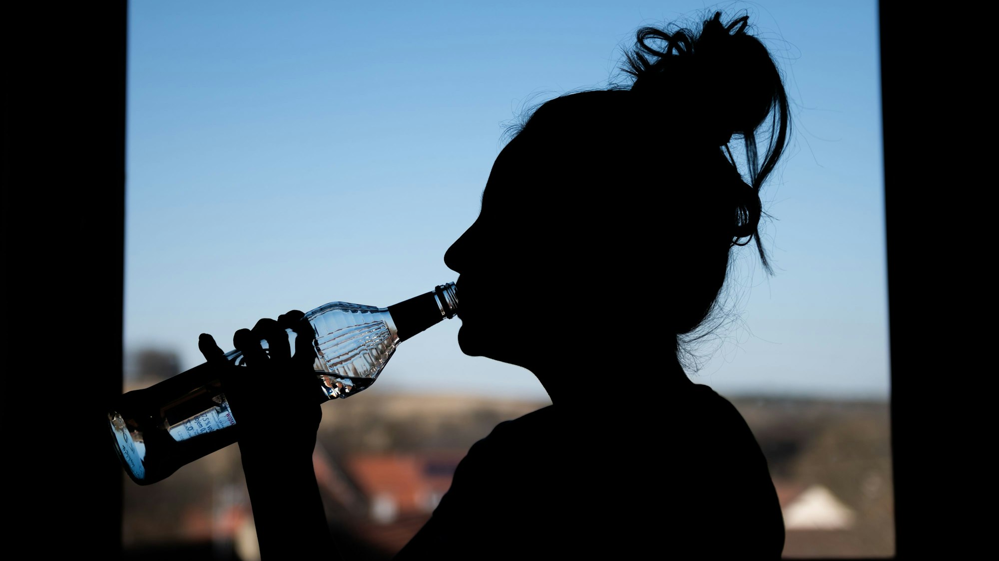 Schatten einer weiblichen Person, die in einem Zimmer vor dem Fenster aus einer Flasche Wodka trinkt.