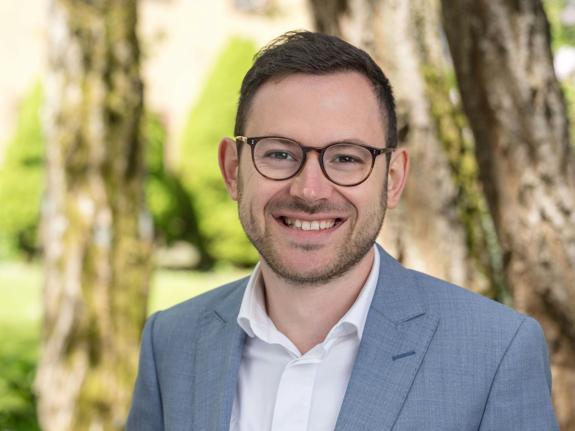 Porträtbild von Emmanuel Kunz, der ein helles Hemd mit einem blauen Sakko trägt.