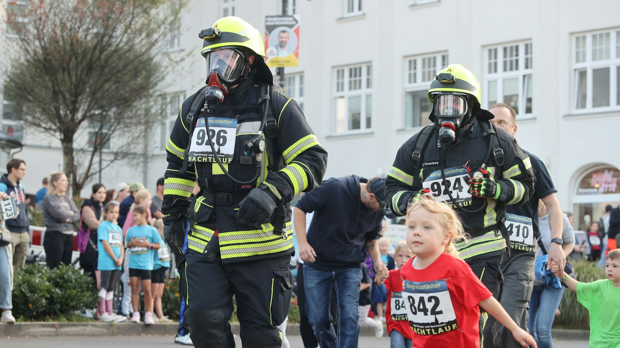 Zu sehen sind Feuerwehrleute in Uniform, die sich unter die Kinder eines Volkslaufes gemischt haben.
