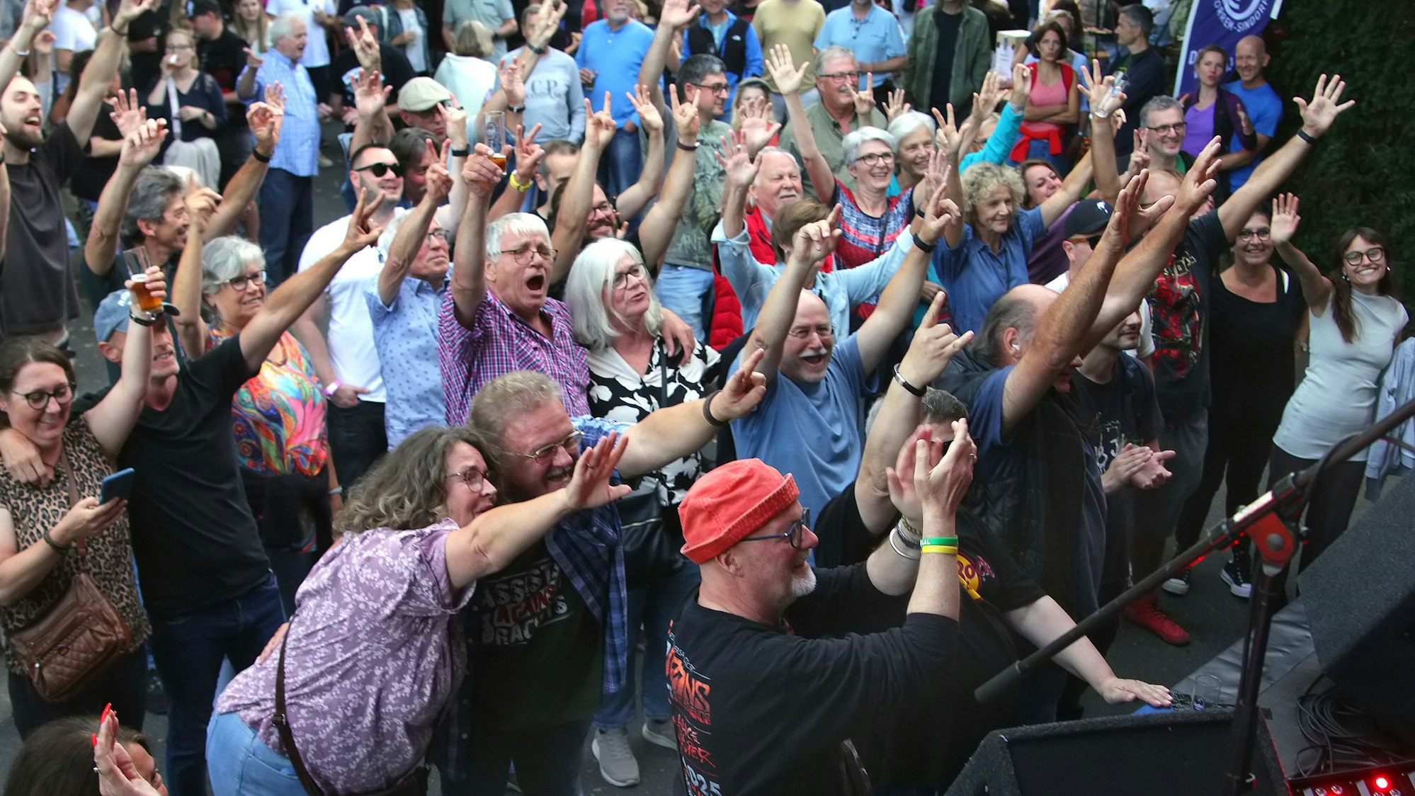 Das Bild zeigt das Publikum, das mit erhobenen Händen der Bühne zugewandt ist.