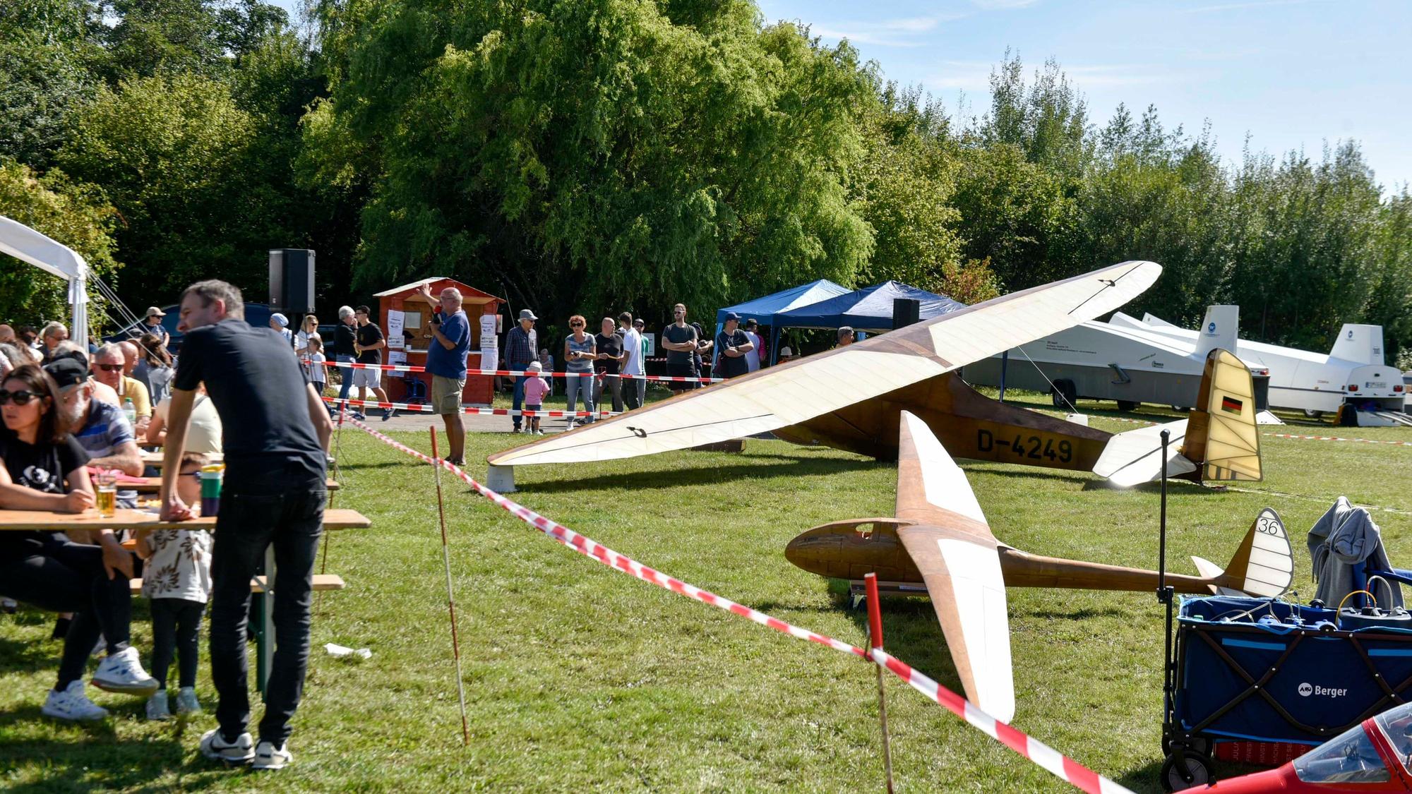 Das Bild zeigt zahlreiche Menschen auf der Wiese, und daneben einige Segelflugzeuge.