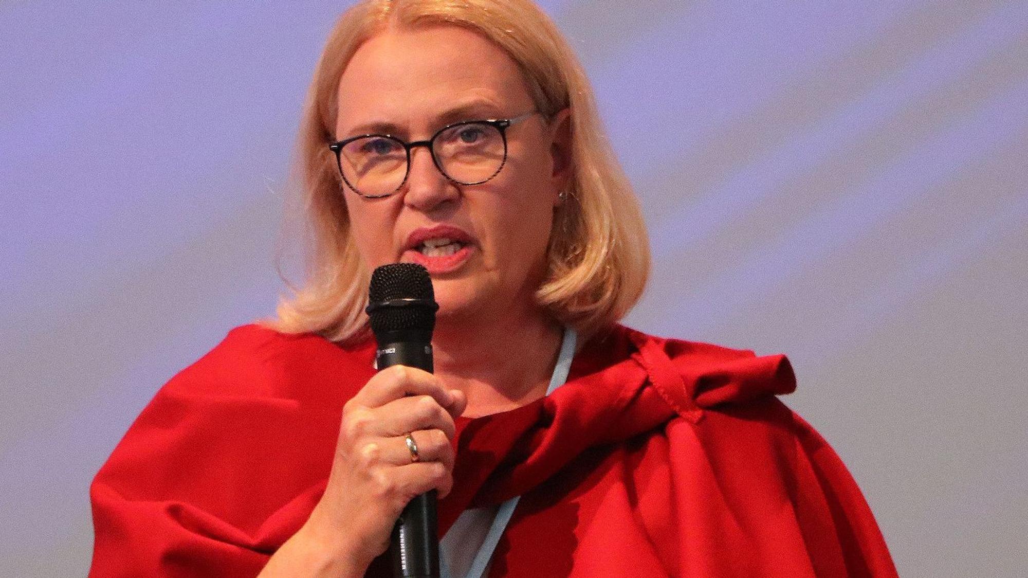 Auf dem Bild ist das Portrait einer Frau zu sehen, sie hält ein Mikrofon in der Hand.